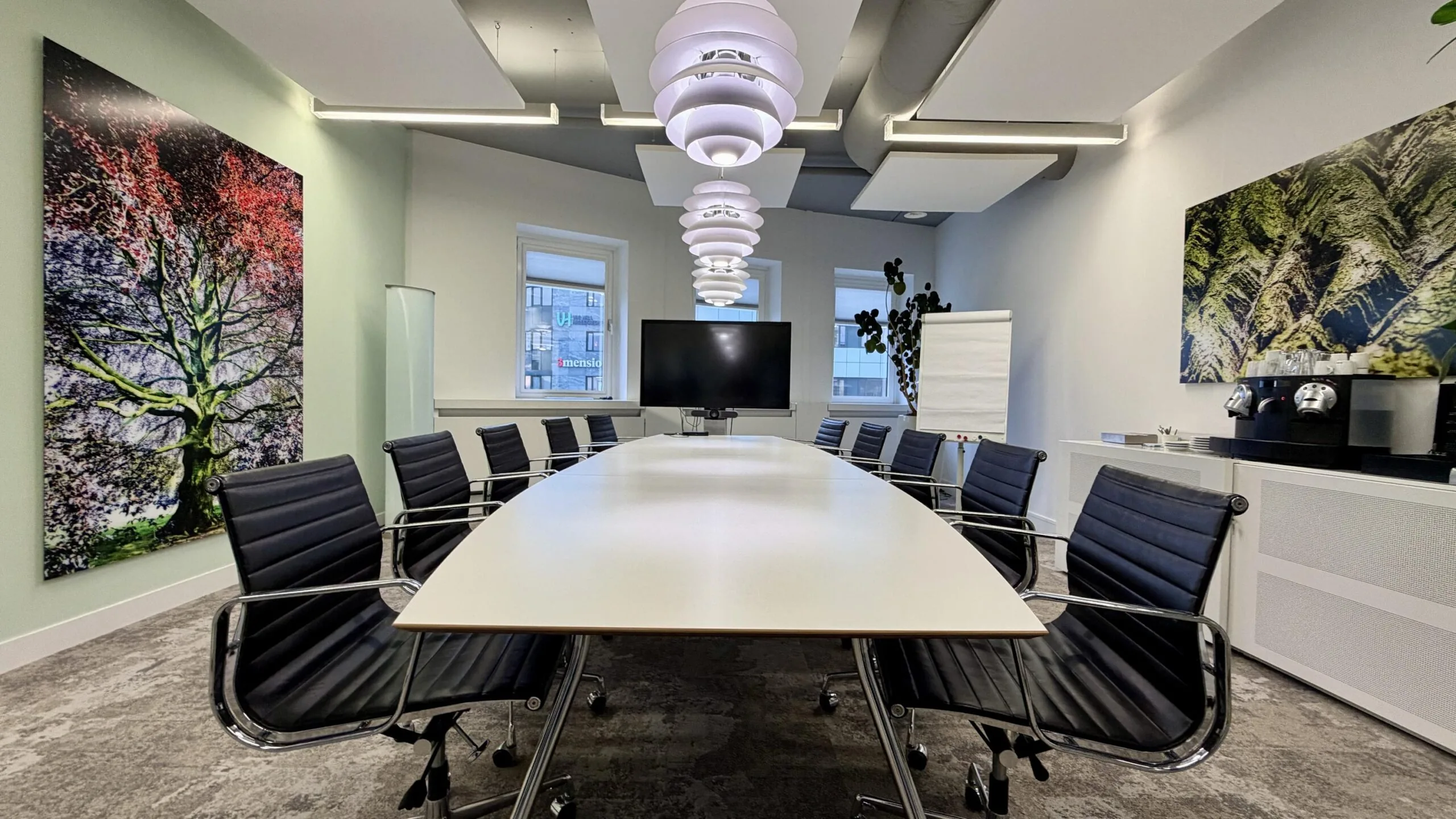 Moderne vergaderruimte aan de Euclideslaan met een lange tafel, leren stoelen, een scherm, koffiezetapparaat en grote muurkunst.
