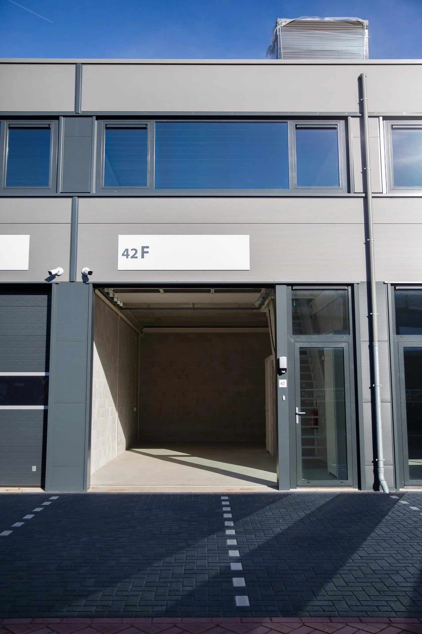 Grijze bedrijfsunit met open garage en glazen deur op huisnummer 42F aan de Laan van s-Gravenmade.
