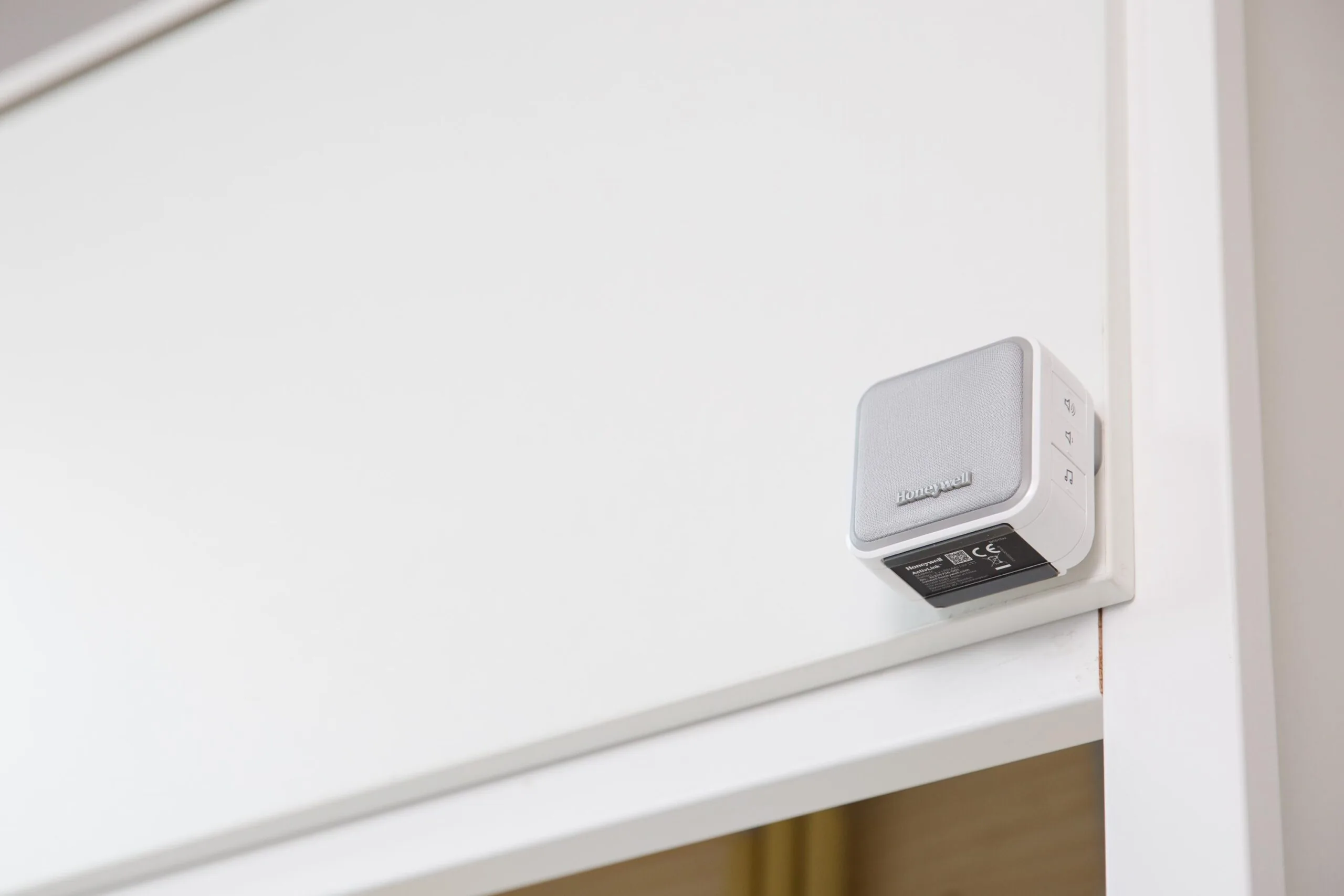 Een witte Honeywell deurbel is gemonteerd boven een deuropening in een modern interieur.