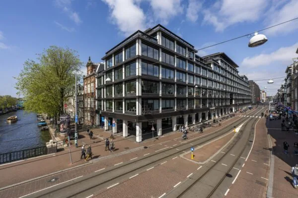 Straatbeeld van de Vijzelstraat in Amsterdam met moderne en historische gebouwen langs de gracht.