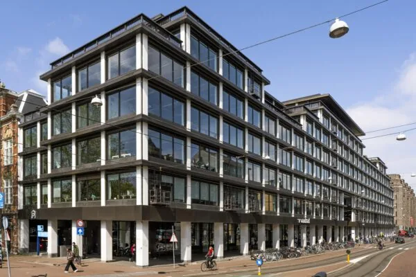 Modern kantoorgebouw aan de Vijzelstraat in Amsterdam met grote glazen gevel en fietsen voor de ingang.