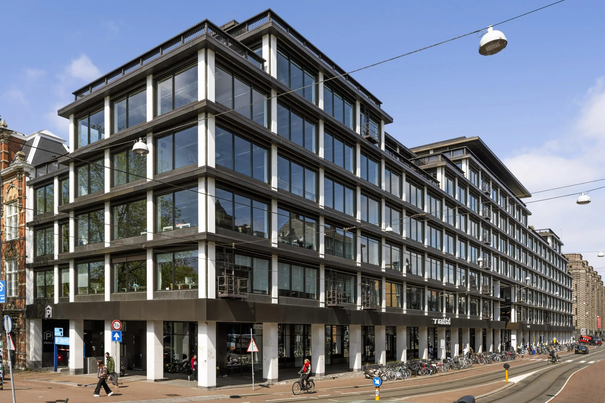 Modern kantoorgebouw aan de Vijzelstraat in Amsterdam met grote glazen gevel en fietsen voor de ingang.