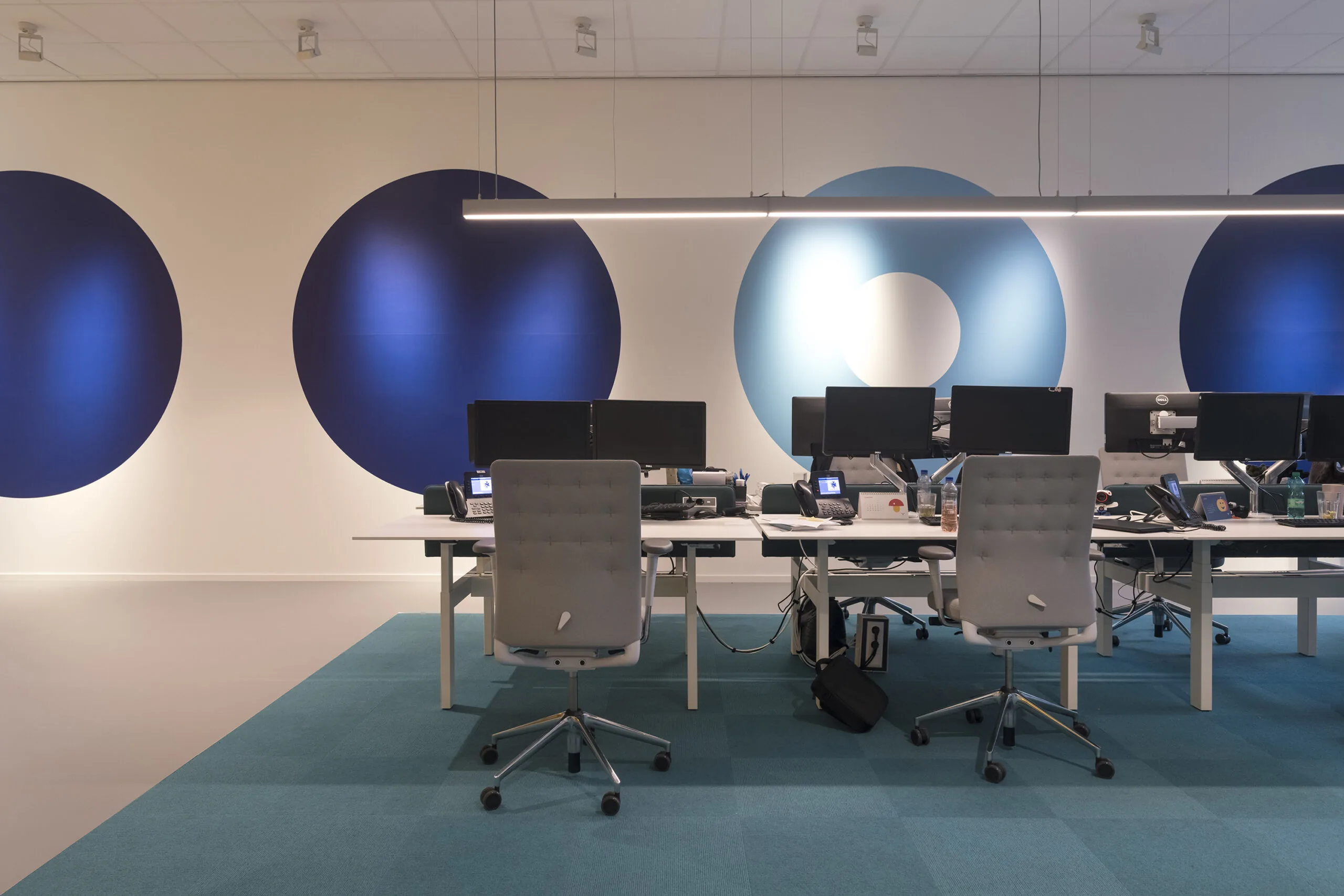 Modern kantoorinterieur aan de Vijzelstraat met bureaus, bureaustoelen en grote blauwe cirkelvormige muurdecoratie.