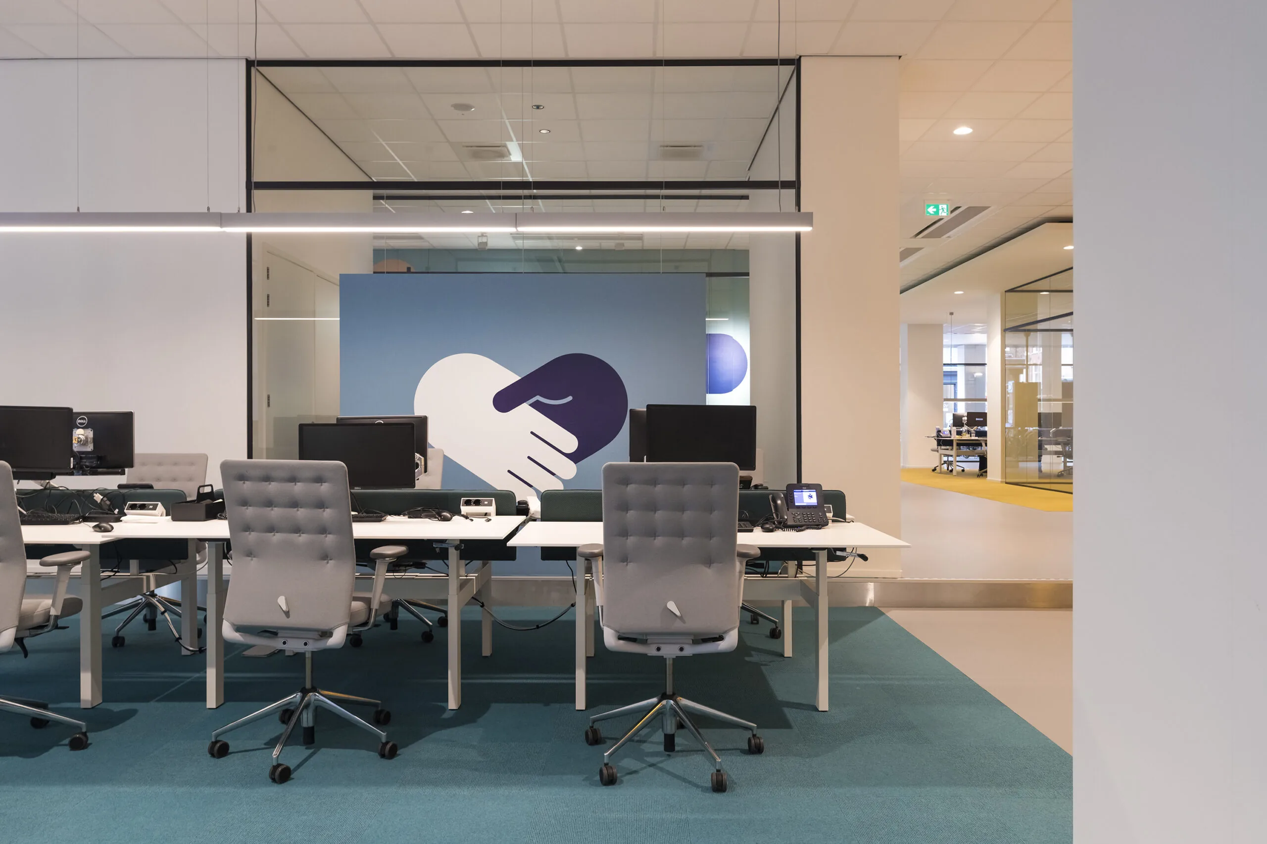 Moderne kantoorruimte aan de Vijzelstraat met bureaus, bureaustoelen, computers en een muurschildering van twee handen die elkaar schudden.