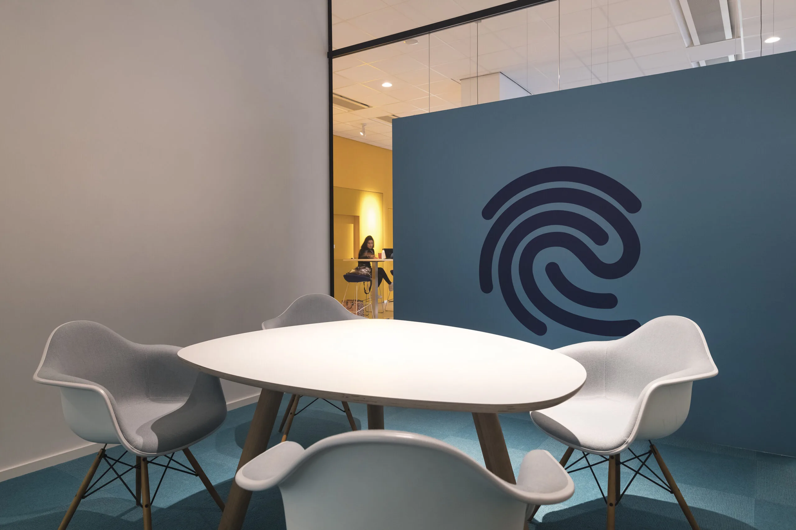 Moderne vergaderruimte met witte tafel, vier stoelen en een blauwe wand met een groot vingerafdruklogo in een kantoorpand aan de Vijzelstraat.
