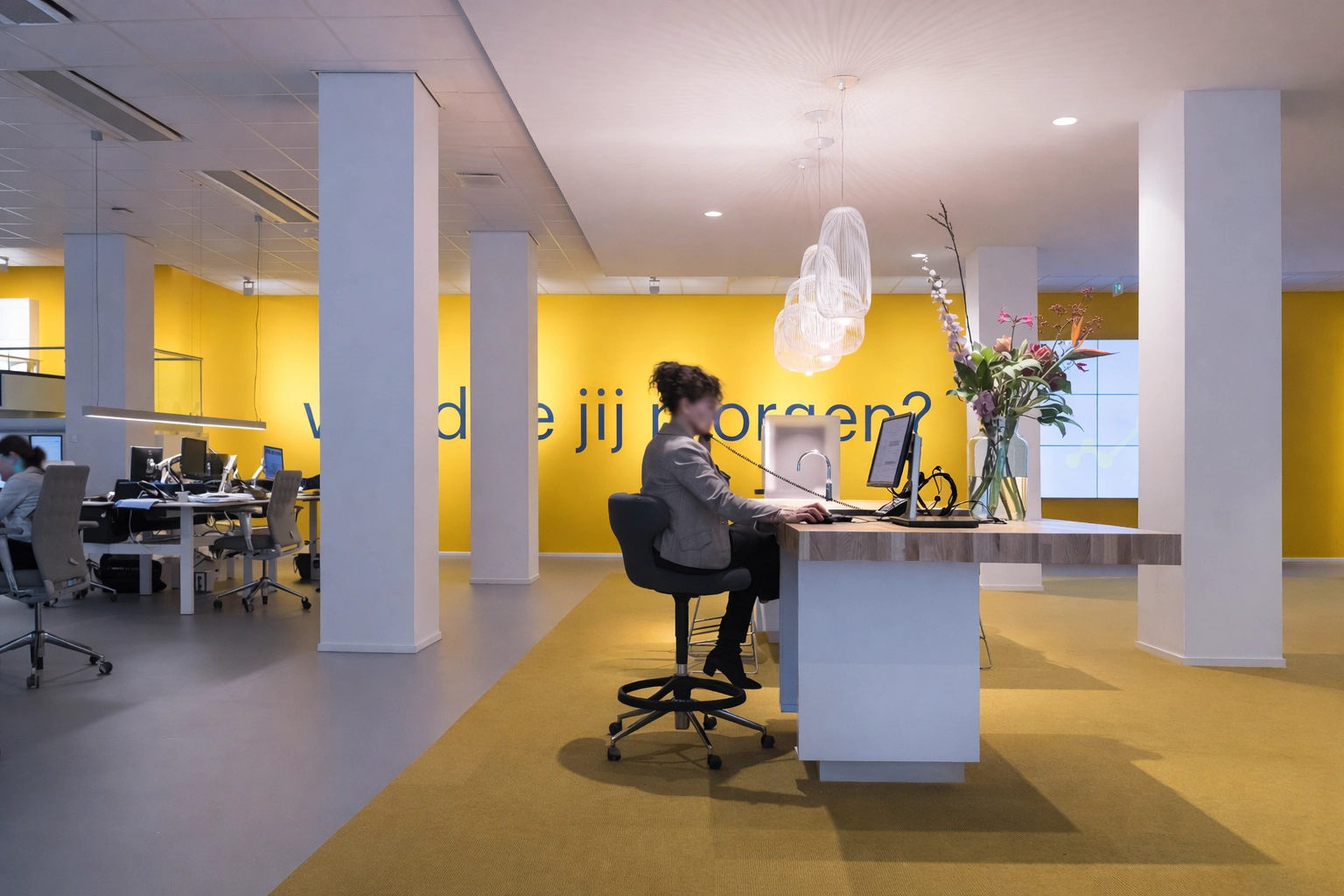Moderne kantoorruimte aan de Vijzelstraat met een receptioniste achter een balie en een felgele muur met de tekst "wie ben jij morgen?".