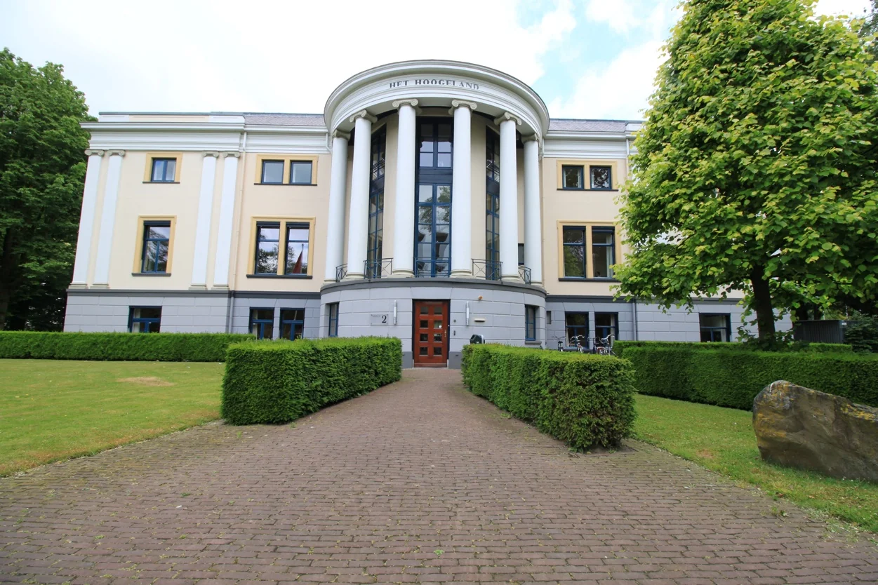 Vooraanzicht van het statige gebouw 'Het Hoogeland' aan de Museumlaan, omgeven door een verzorgde tuin met heggen en bomen.
