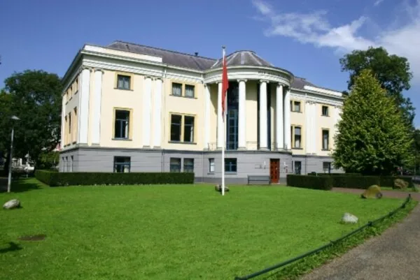 Gele klassiek ogende villa met witte zuilen aan de Museumlaan, omringd door een groen gazon en bomen.