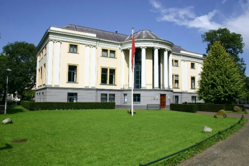 Gele klassiek ogende villa met witte zuilen aan de Museumlaan, omringd door een groen gazon en bomen.