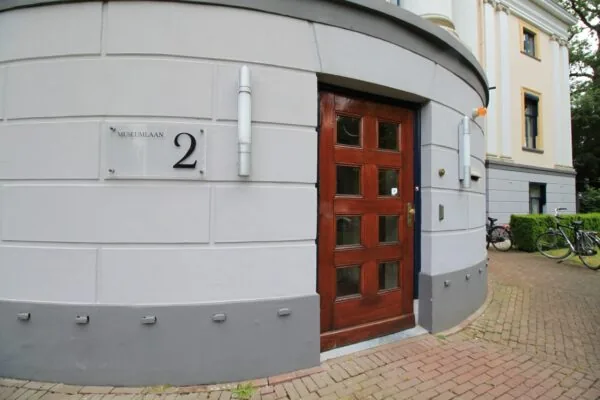 Ingang van een klassiek gebouw aan de Museumlaan 2 met houten deur en gevelbord.