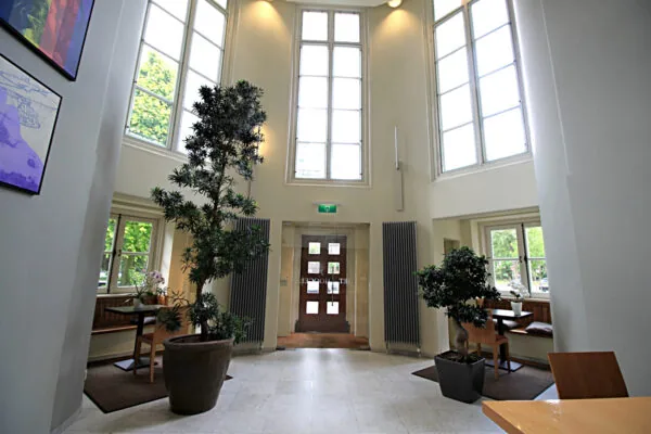 Lichte en hoge entreehal met grote ramen, planten en zithoeken in Museumlaan.