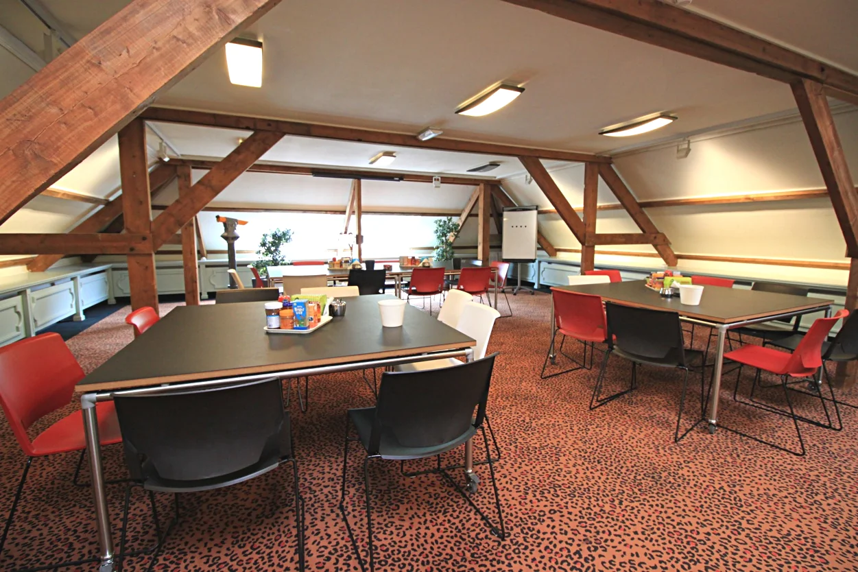 Vergaderruimte op Museumlaan met houten balken, kleurrijke stoelen en tafels met drankjes en snacks.