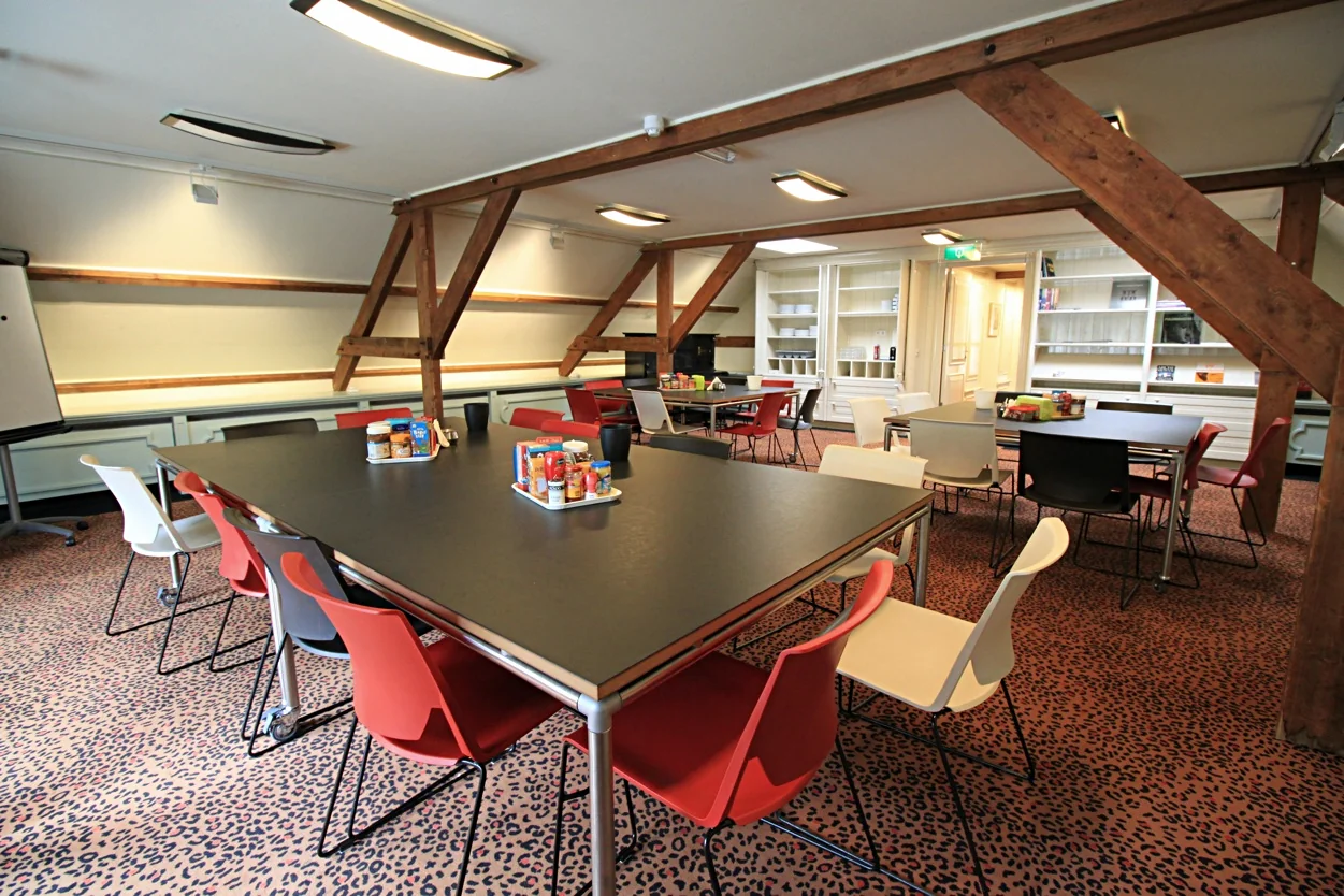 Vergaderruimte aan de Museumlaan met meerdere tafels, kleurrijke stoelen en hapjes op tafel in een sfeervolle ruimte met houten balken.
