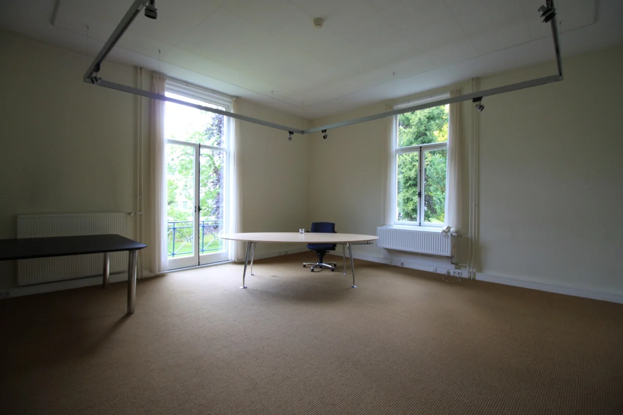 Licht kantoor met grote ramen, een enkel bureau, bureaustoel en uitzicht op groen vanaf de Museumlaan.