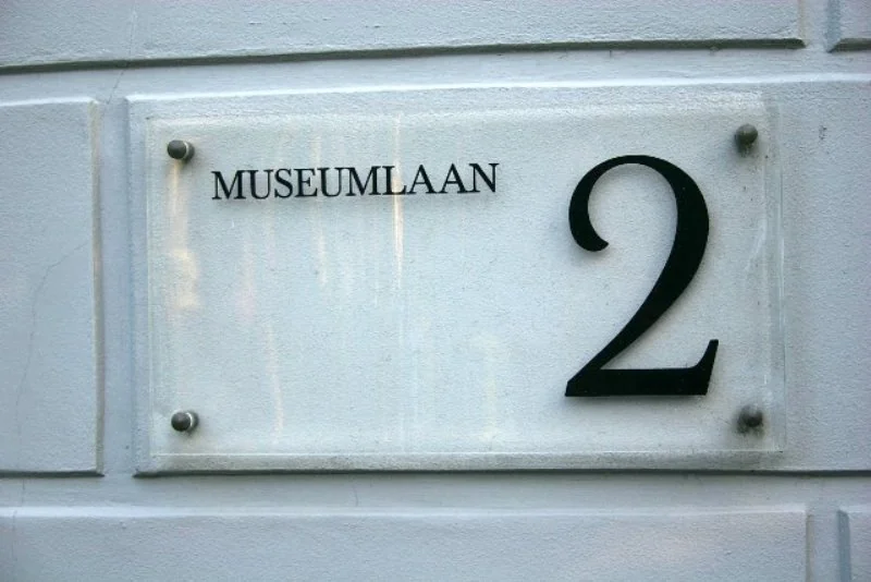 Wit naambord met het adres Museumlaan 2 op een gevelmuur.