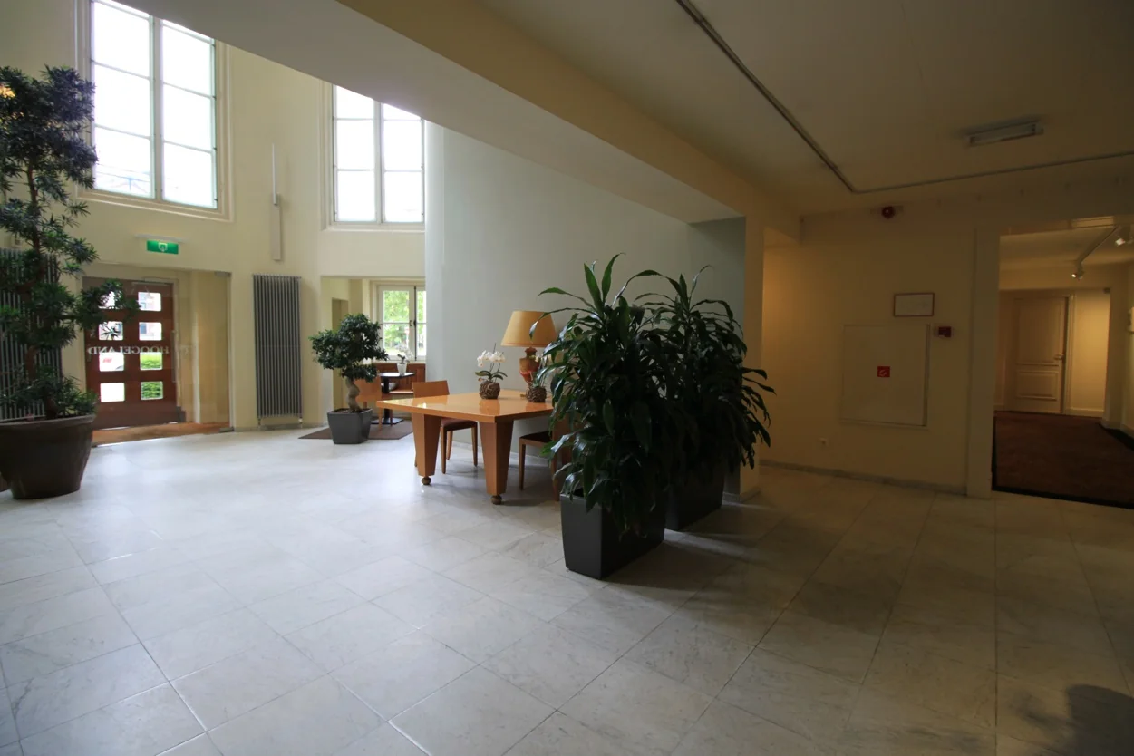 Lichte en ruime hal met grote ramen, planten en een houten tafel aan de Museumlaan.