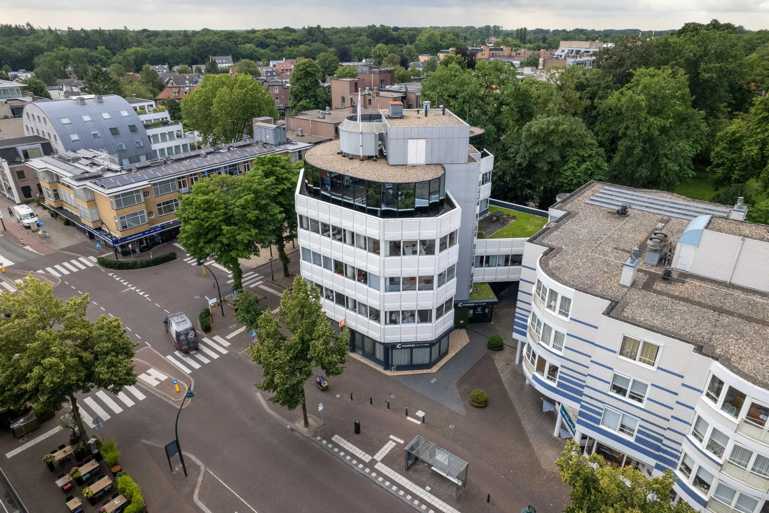 Luchtfoto van het kantoorgebouw aan de 1e Hogeweg in Zeist, omringd door bomen en andere stedelijke bebouwing.