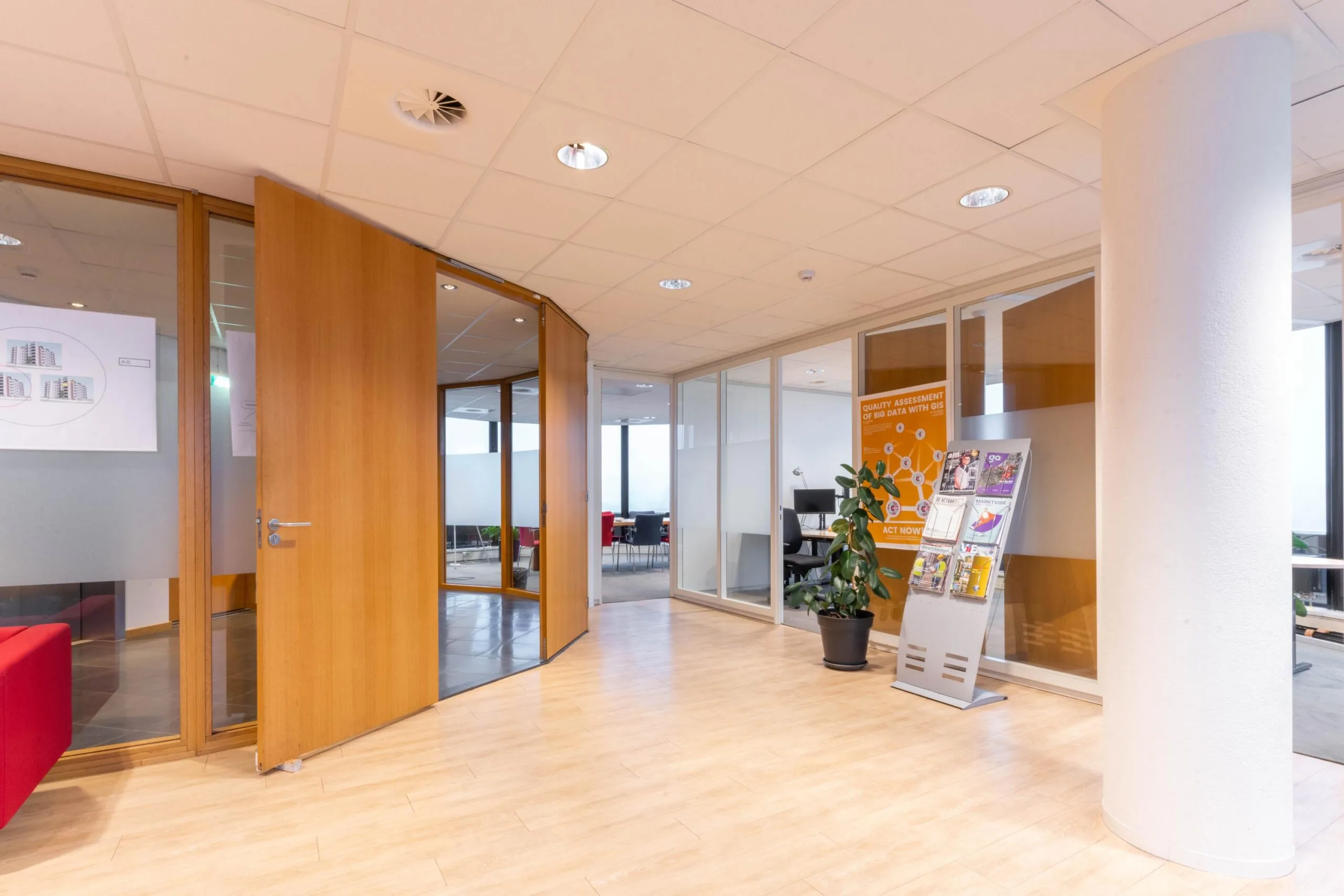 Ingang van een modern kantoor aan de 1e Hogeweg met glazen wanden, houten deuren en een tijdschriftenrek.