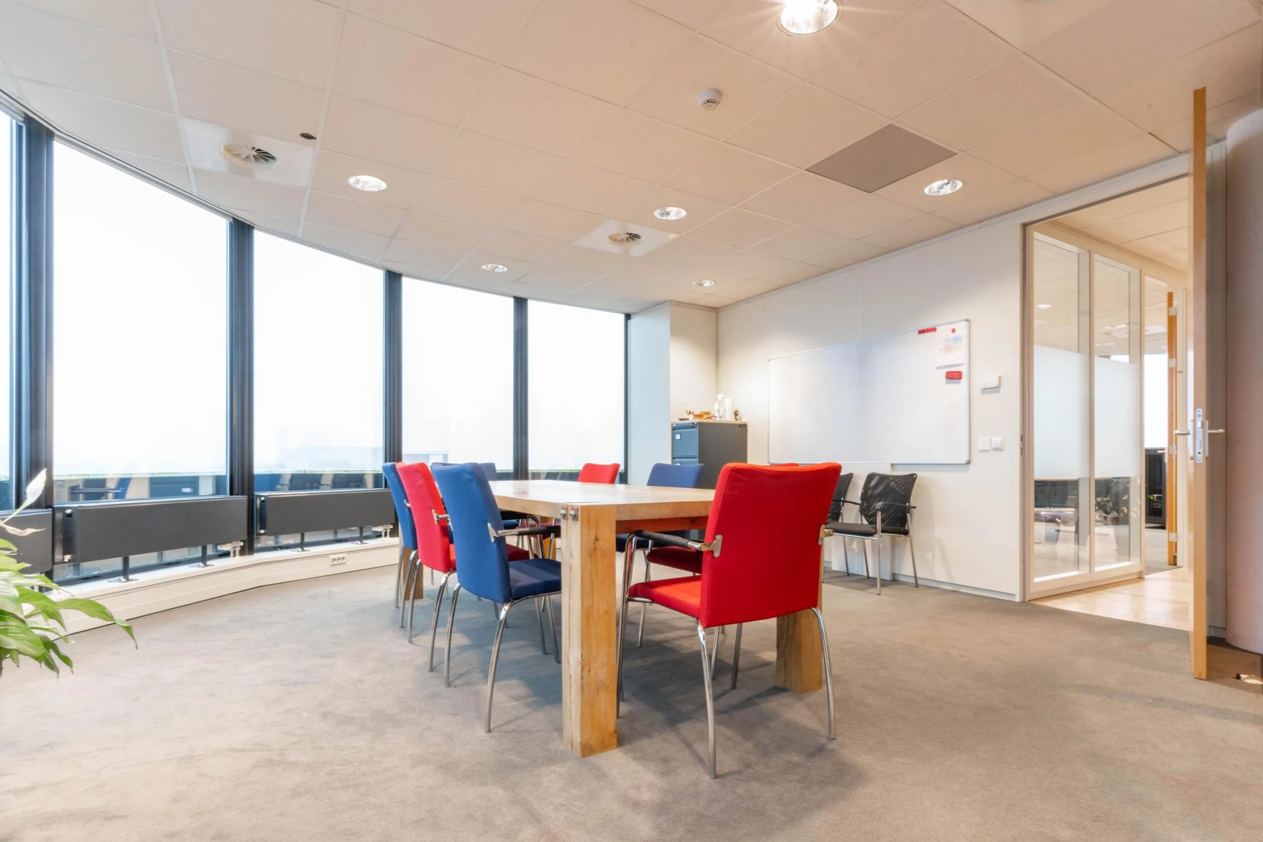 Vergaderruimte met houten tafel, kleurrijke stoelen en grote ramen aan de 1e Hogeweg.