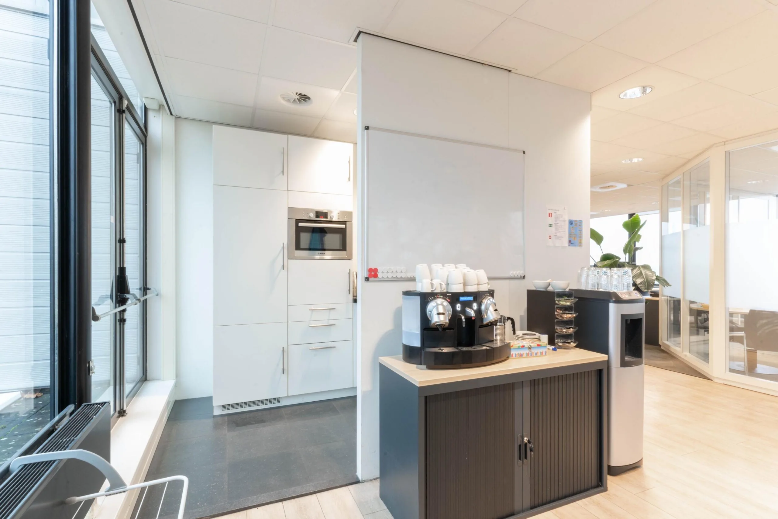 Moderne kantoorkeuken met een koffiemachine, waterautomaat en ingebouwde oven.