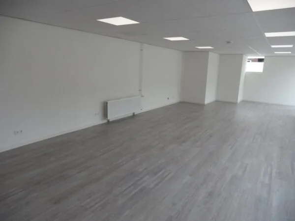Lege, strak afgewerkte ruimte met grijze vloer, witte muren en systeemplafond aan de Jacques Perkstraat.