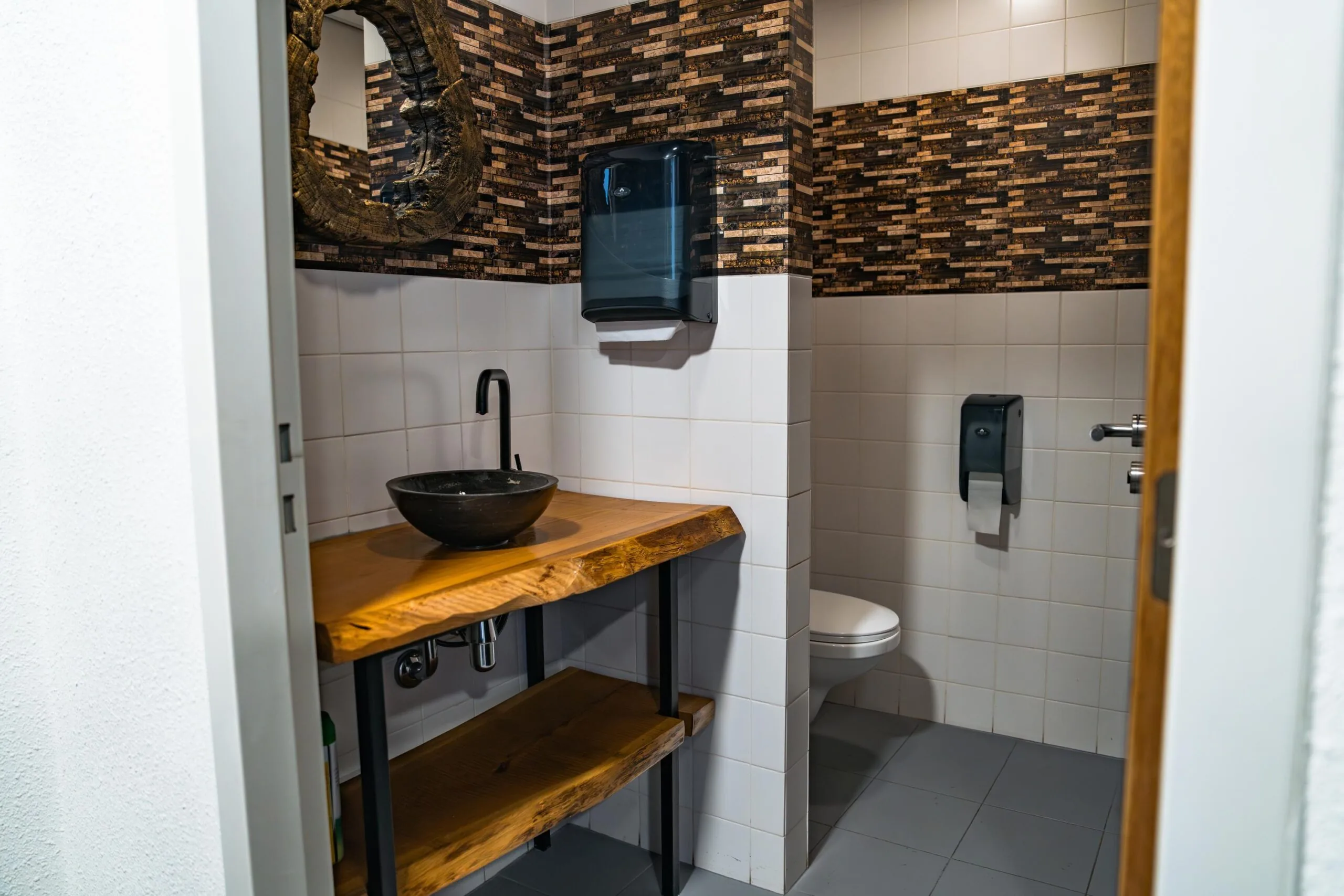 Moderne toiletruimte met een houten wastafelmeubel, een zwarte waskom en mozaïektegels aan de muur in Frankfurtstraat.