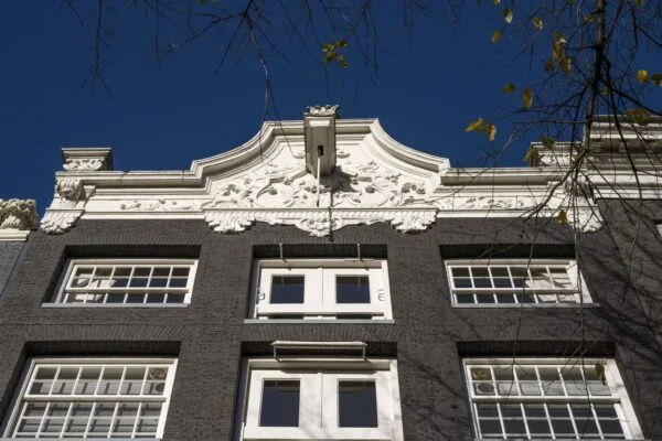 Gevel van een historisch grachtenpand aan de Herengracht met witgepleisterd sierfronton en donkere bakstenen.
