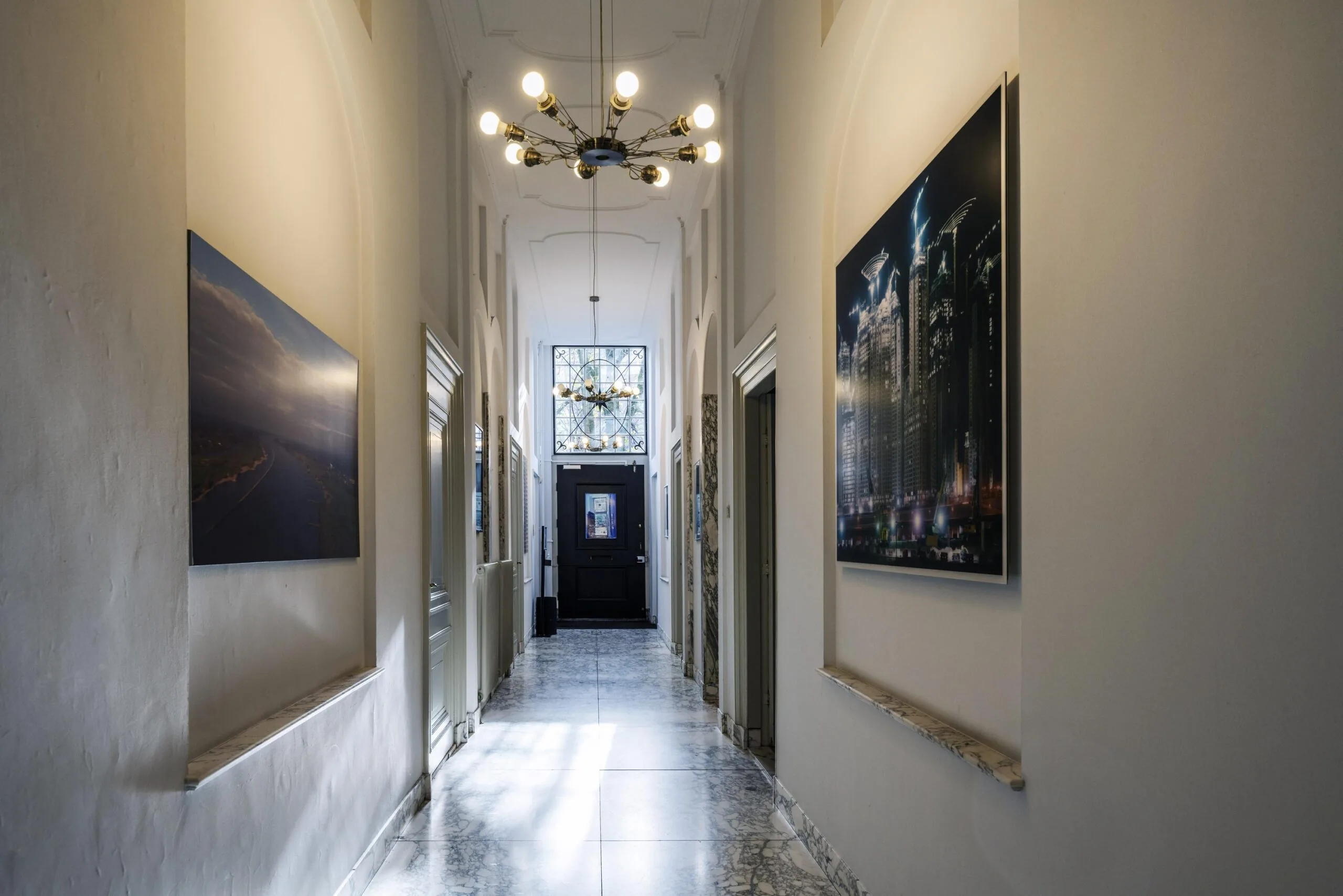 Lichte, klassieke gang in een pand aan de Herengracht met marmeren vloer, moderne plafondlamp en grote fotokunst aan de muren.