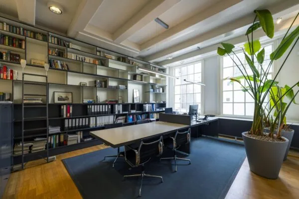 Modern ingericht kantoor aan de Herengracht met grote boekenkast, vergadertafel, werkplek en veel natuurlijk licht.