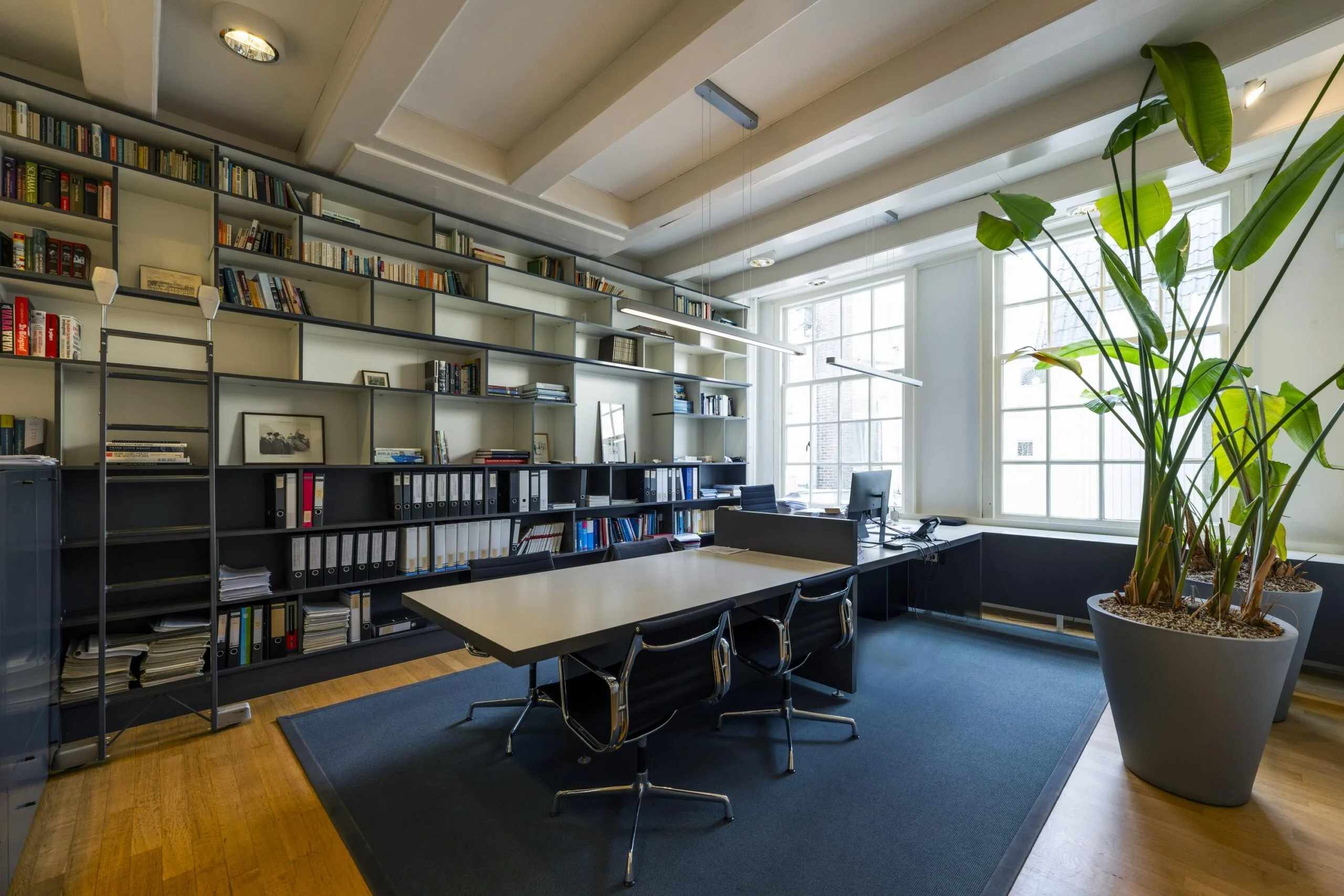 Modern ingericht kantoor aan de Herengracht met grote boekenkast, vergadertafel, werkplek en veel natuurlijk licht.