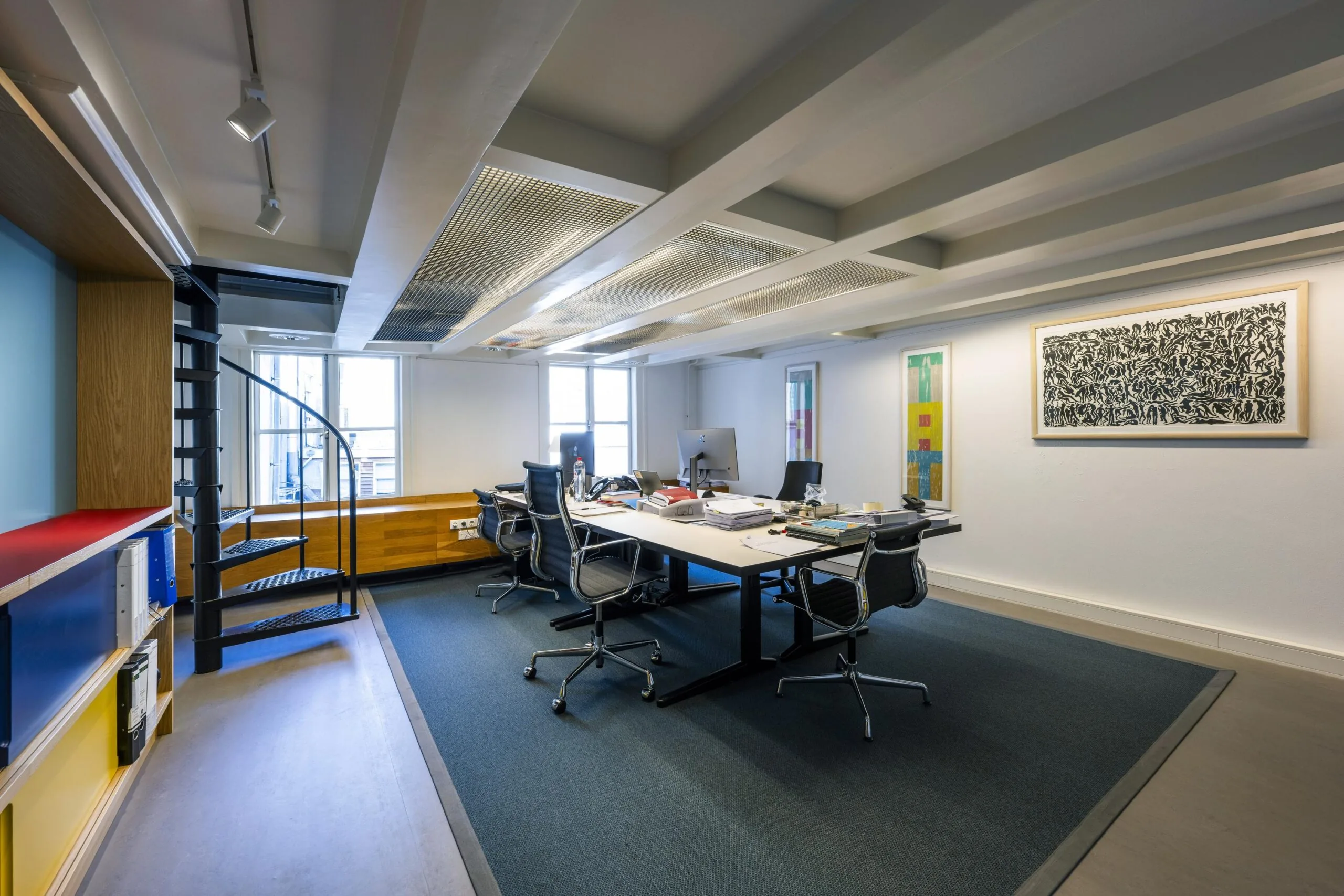 Modern kantoorinterieur aan de Herengracht met een grote werktafel, bureaustoelen, kunst aan de muur en een zwarte spiltrap.