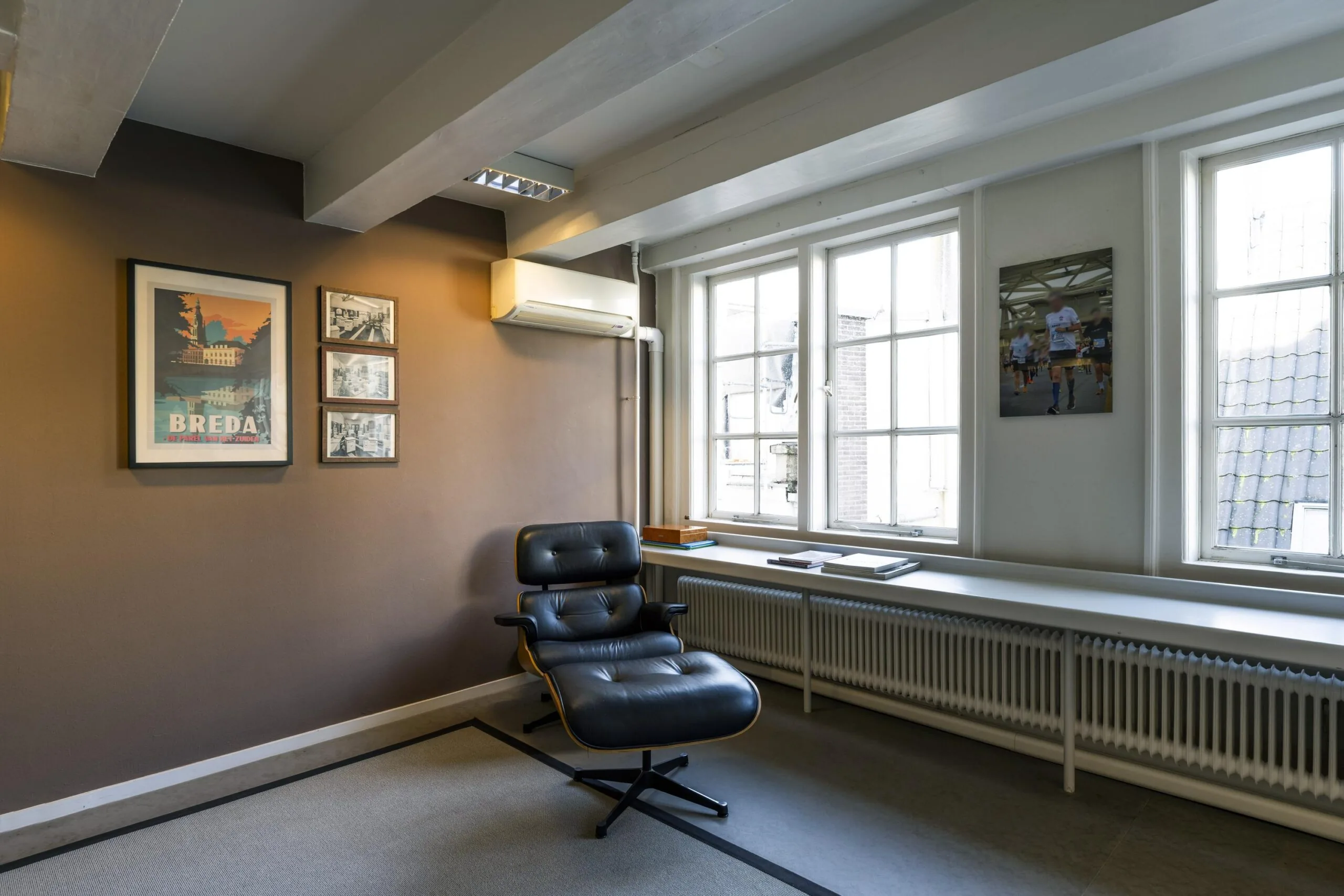 Moderne kantoorruimte aan de Herengracht met een zwarte loungestoel, kunst aan de muur en grote ramen die natuurlijk licht binnenlaten.