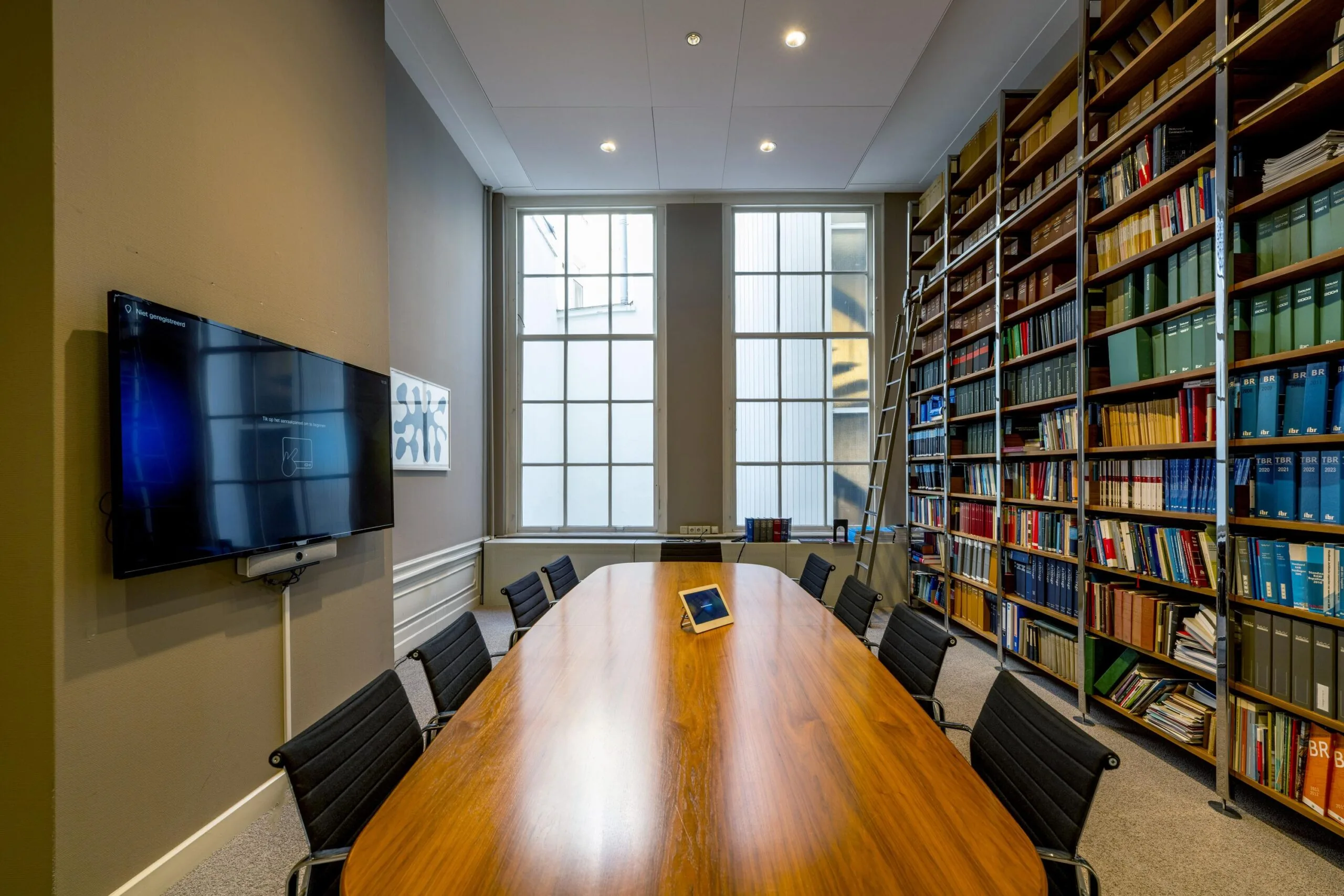 Vergaderruimte aan de Herengracht met lange houten tafel, boekenwand, tv-scherm en grote ramen.