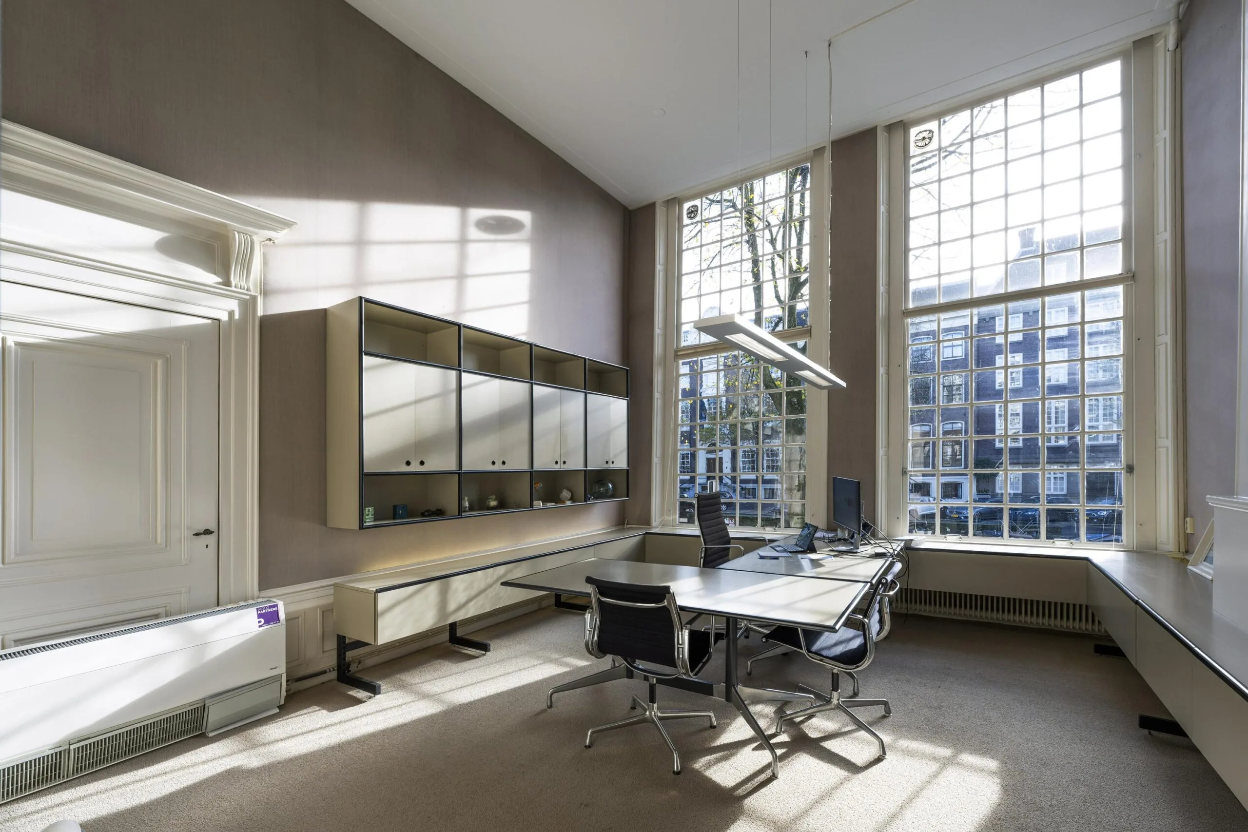 Modern kantoorinterieur aan de Herengracht met grote ramen, strak meubilair en uitzicht op historische Amsterdamse gevels.