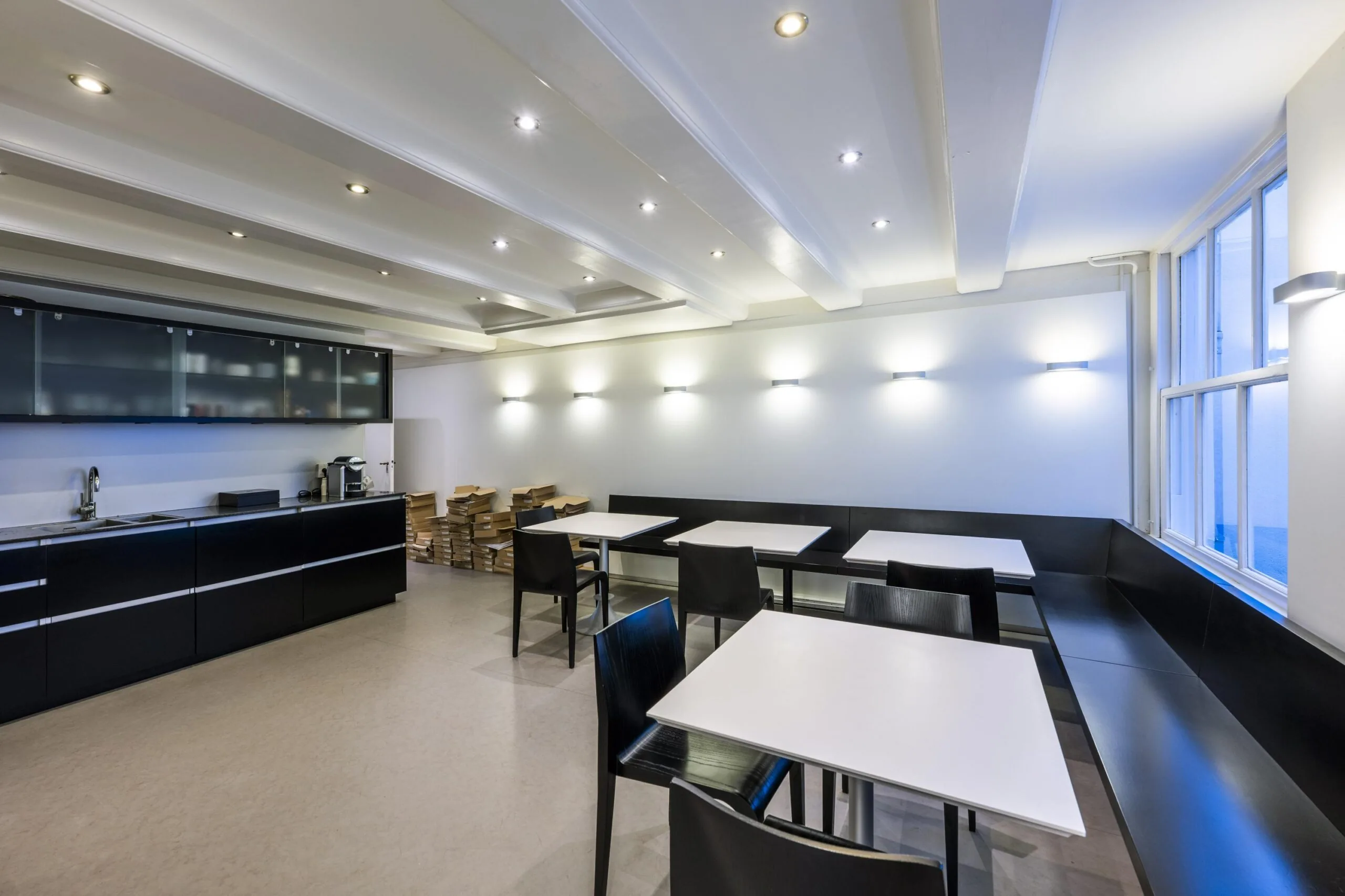 Moderne kantine met zwarte keuken, witte tafels en stapels dossiers langs de muur aan de Herengracht.