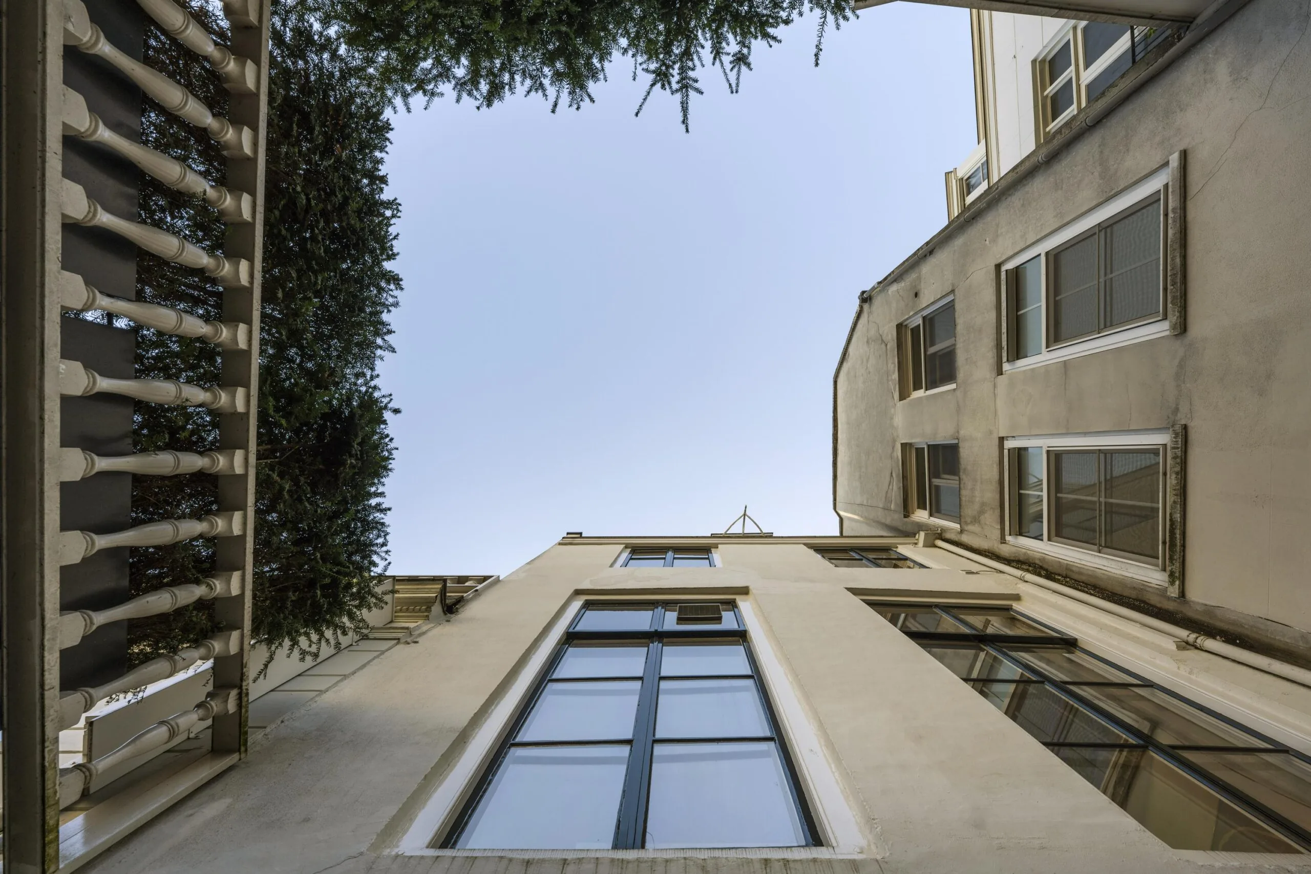 Uitzicht omhoog in een binnentuin aan de Herengracht, omringd door hoge gevels en een balkon met balustrade.