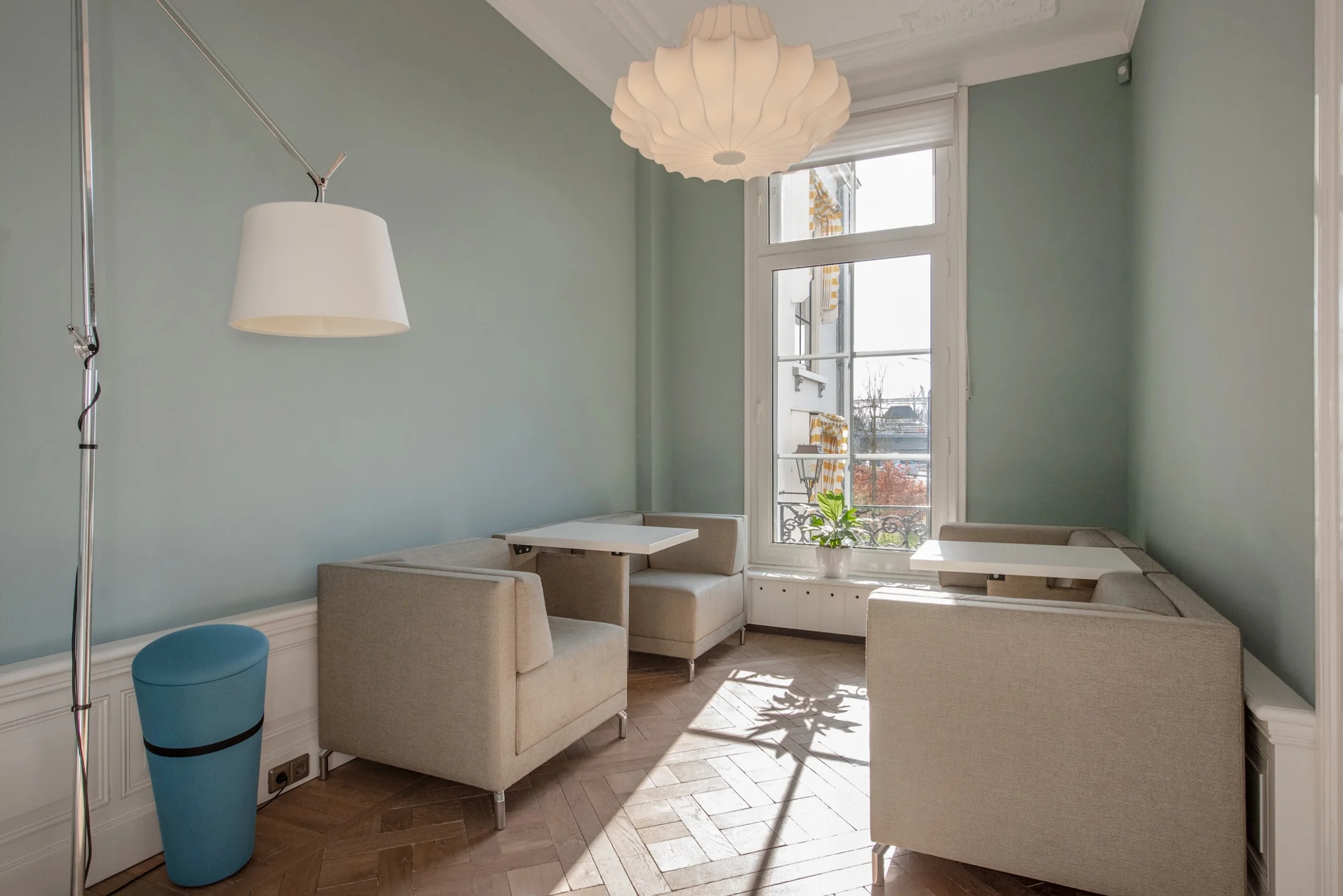Zonnige zithoek met beige banken en witte tafels aan de Jan Thijssenweg, in een lichte kamer met hoge ramen en houten vloer.