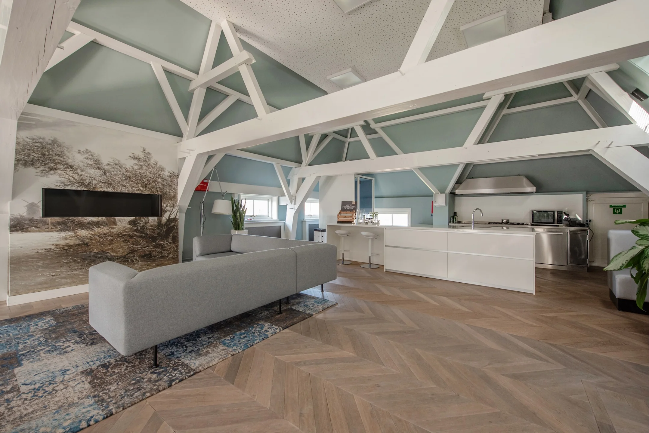Modern ingerichte loft op de Jan Thijssenweg met open keuken, houten visgraatvloer en zitgedeelte onder een karakteristiek balkenplafond.