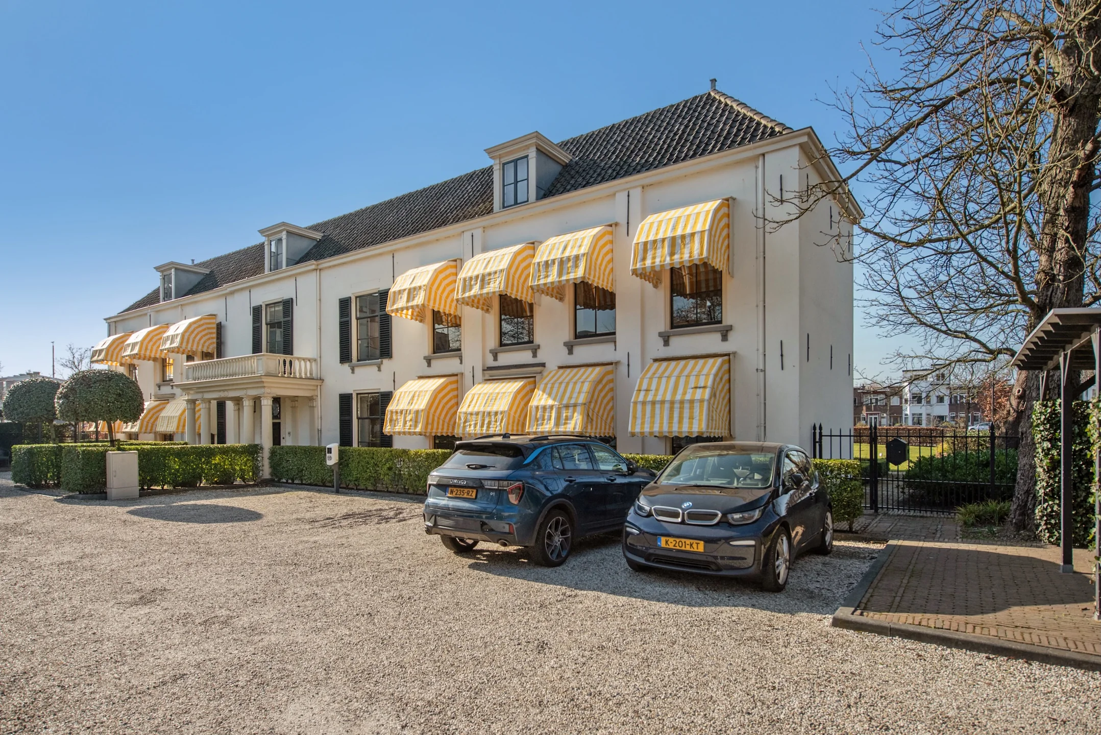 Wit herenhuis aan de Jan Thijssenweg met geel-witte zonneschermen en twee geparkeerde auto's op de oprit.