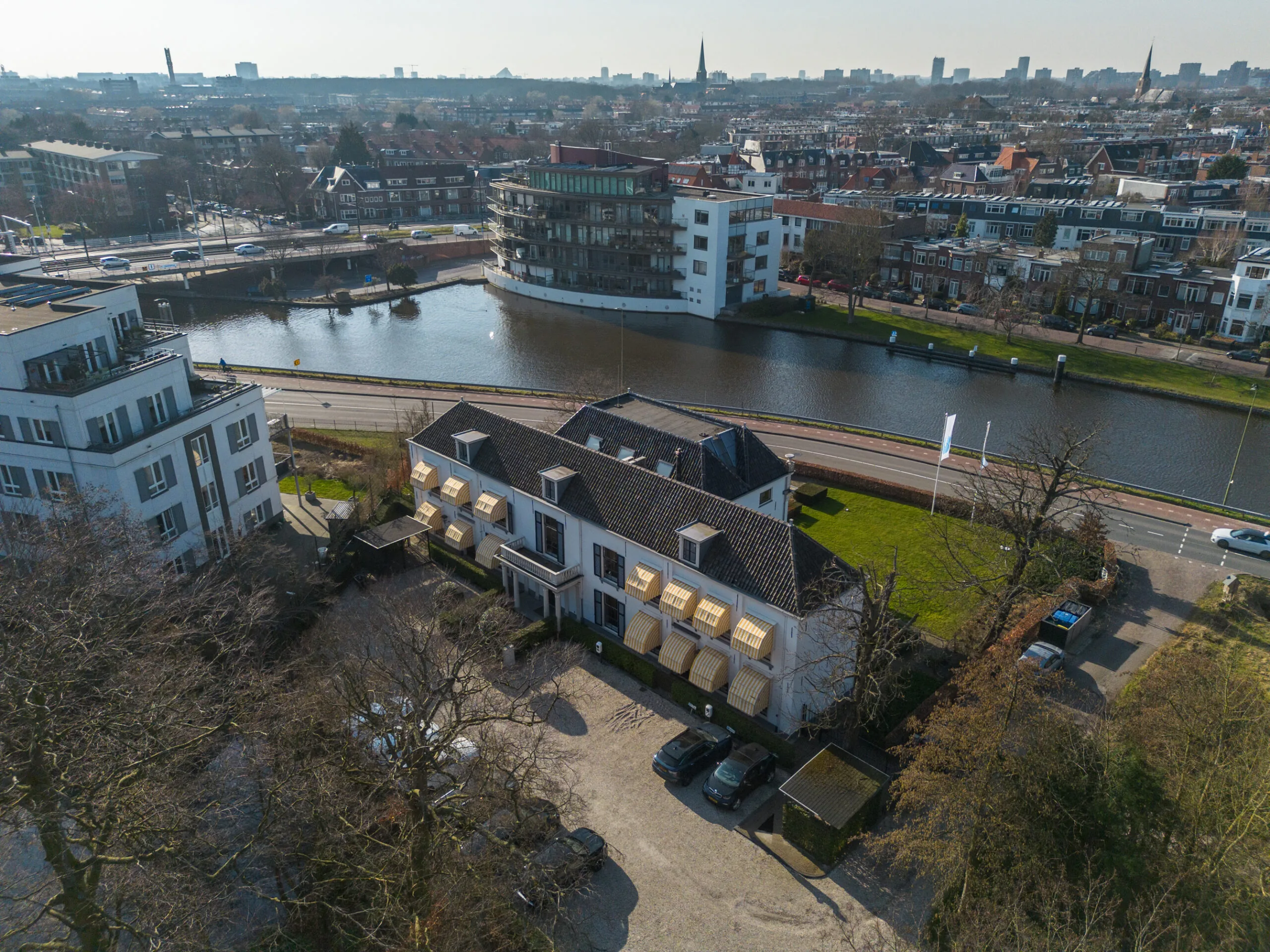 Luchtfoto van een wit gebouw aan de Jan Thijssenweg, gelegen naast een waterkanaal in een stedelijke woonwijk.