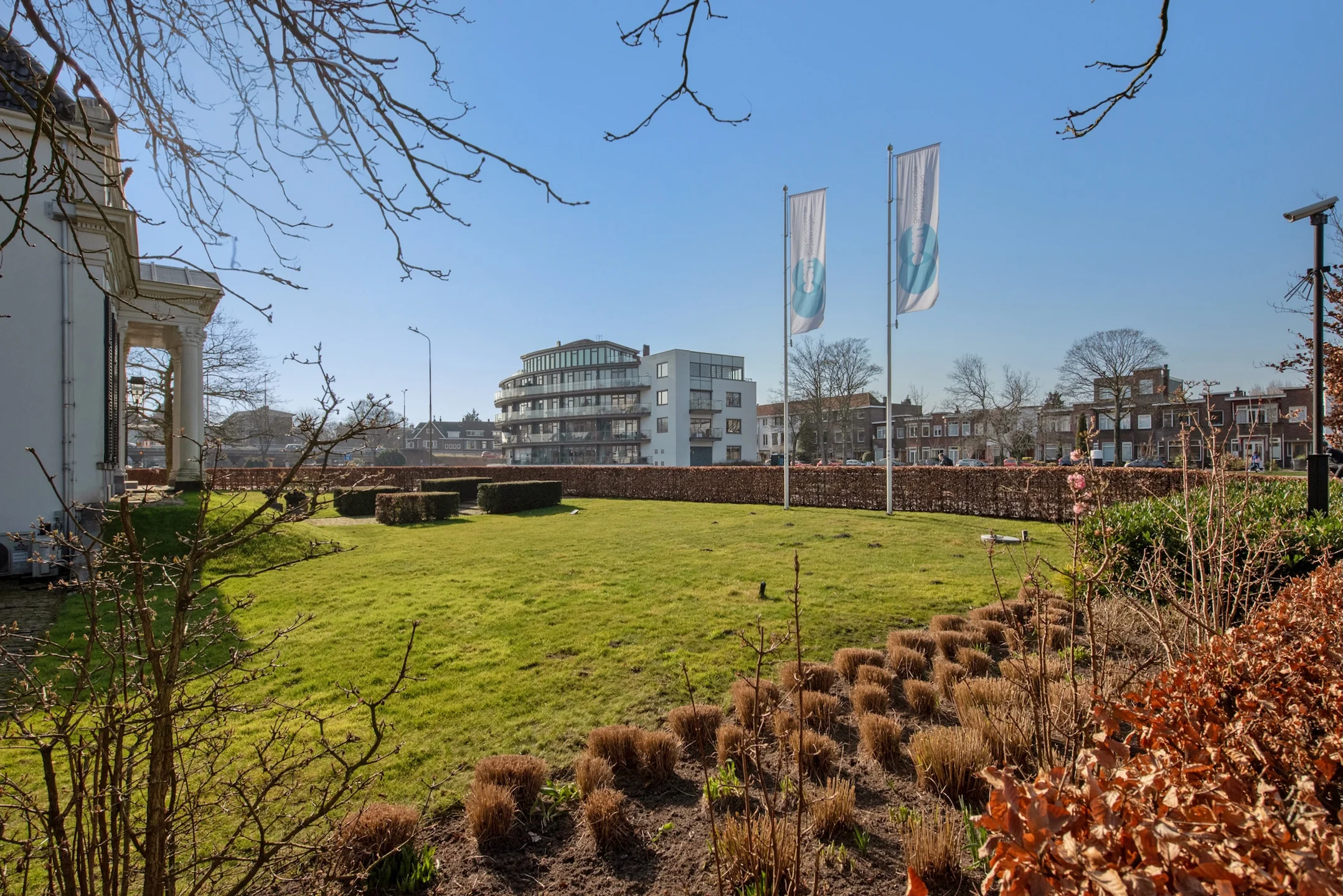 Goed onderhouden tuin aan de Jan Thijssenweg met op de achtergrond een modern appartementencomplex en twee wapperende vlaggen.