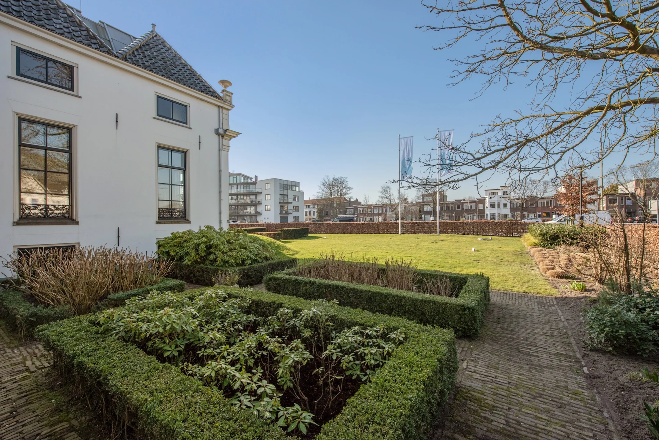Tuin met strak gesnoeide hagen naast een wit herenhuis aan de Jan Thijssenweg met uitzicht op moderne appartementen.