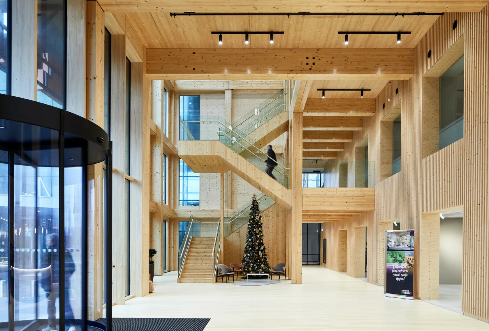 Houten entreehal van het kantoorgebouw aan de Basisweg met een centrale trap, glazen draaideur en versierde kerstboom.