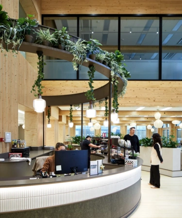 Receptie en koffiebar in een modern houten kantoorgebouw aan de Basisweg, met stijlvolle verlichting en hangplanten.