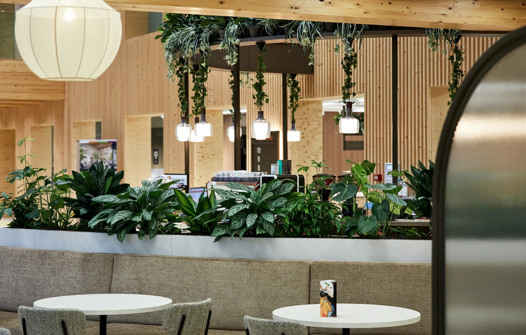 Modern interieur van een koffiebar aan de Basisweg met veel groen, houten accenten en ronde zittafels.