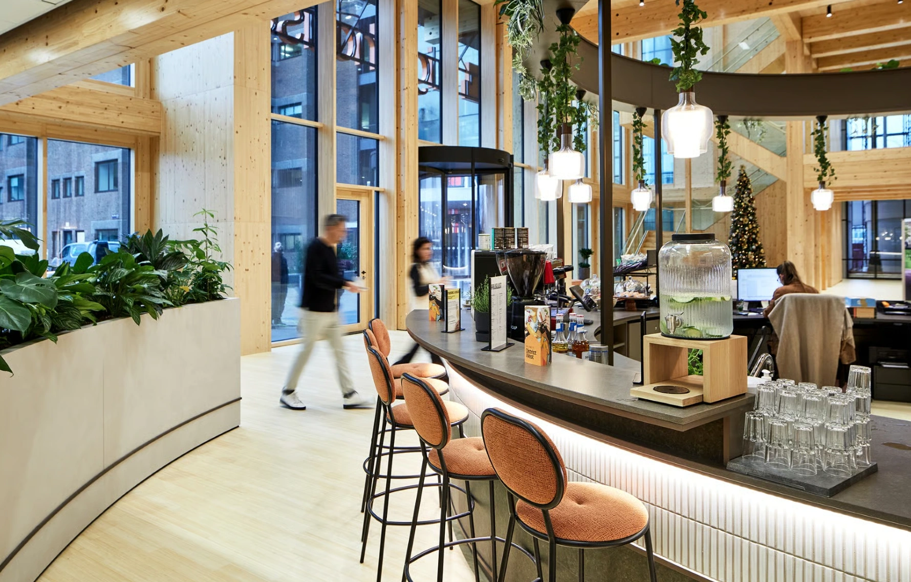 Modern interieur van een kantoor aan de Basisweg met een koffiebar, planten, houten accenten en mensen in beweging.