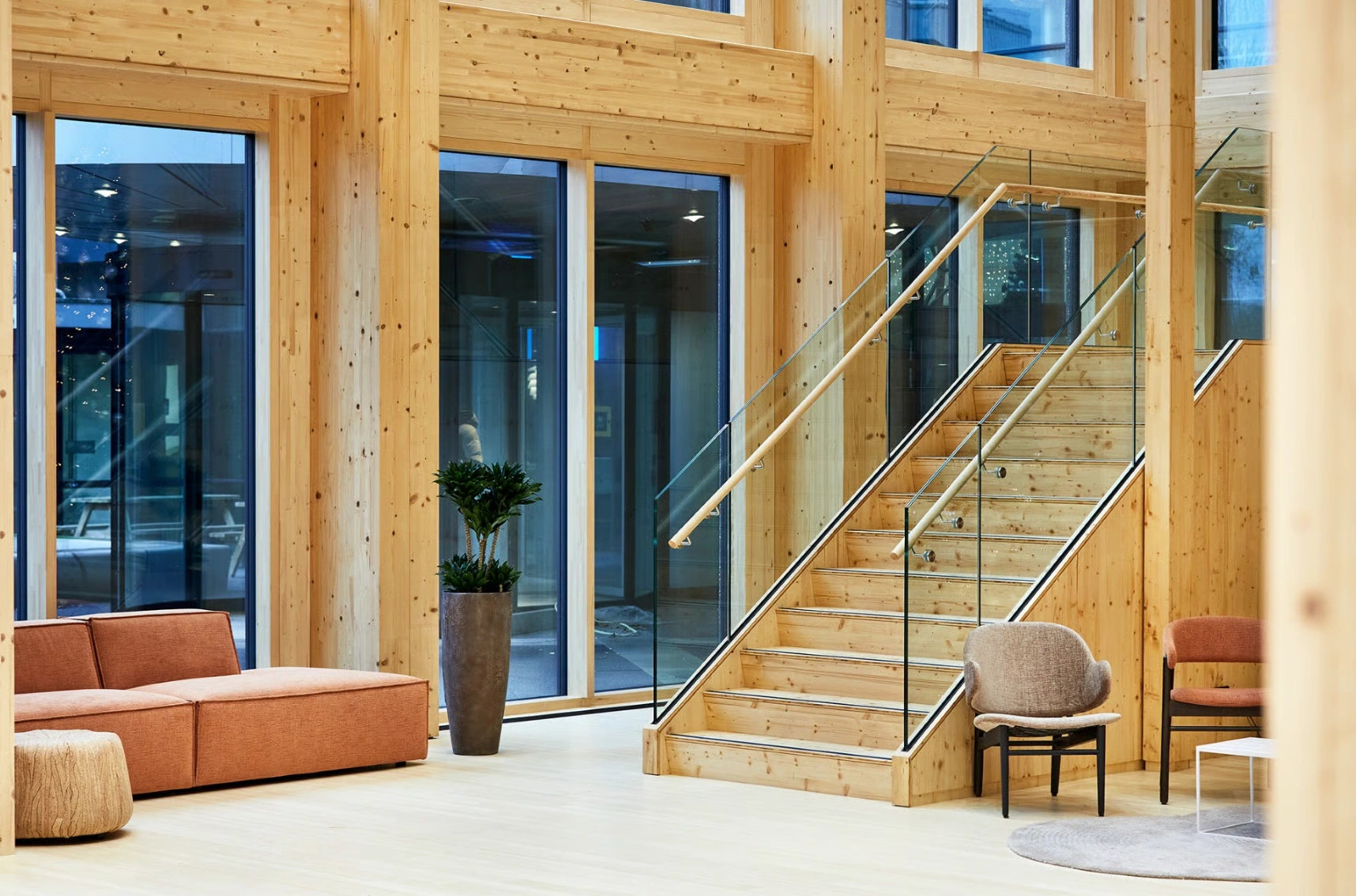 Moderne, houten lobby aan de Basisweg met een glazen trap, zitmeubels en grote ramen.