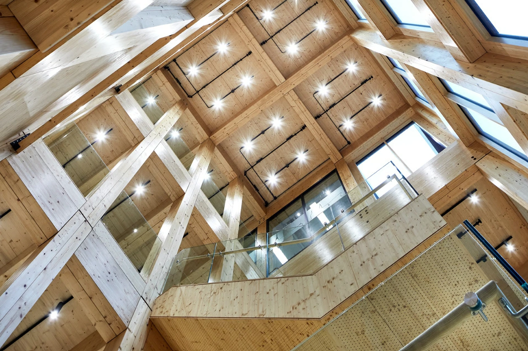 Houten interieur van een atrium op Basisweg 10 met glazen balustrades en plafondverlichting, gezien van onderaf.