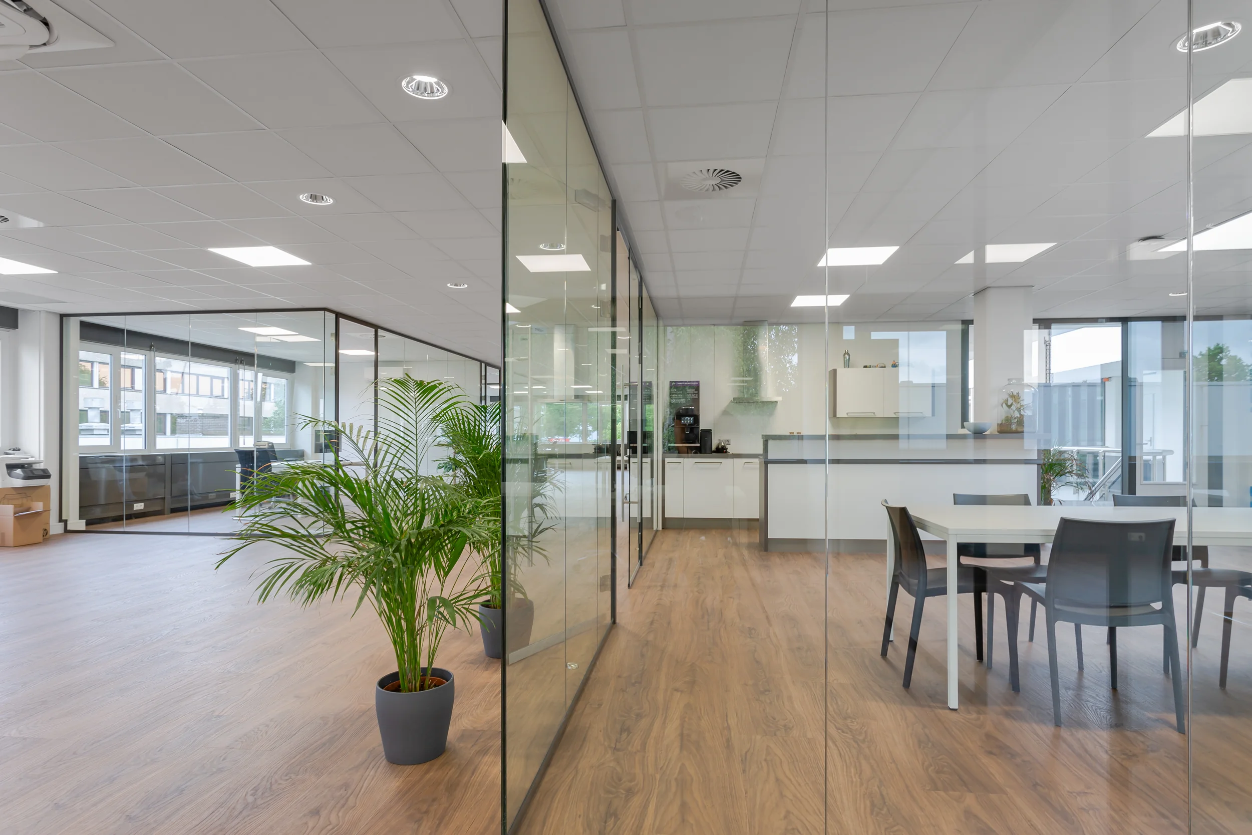 Moderne kantoorruimte aan de Energieweg met glazen wanden, houten vloer, een zithoek en een keuken.