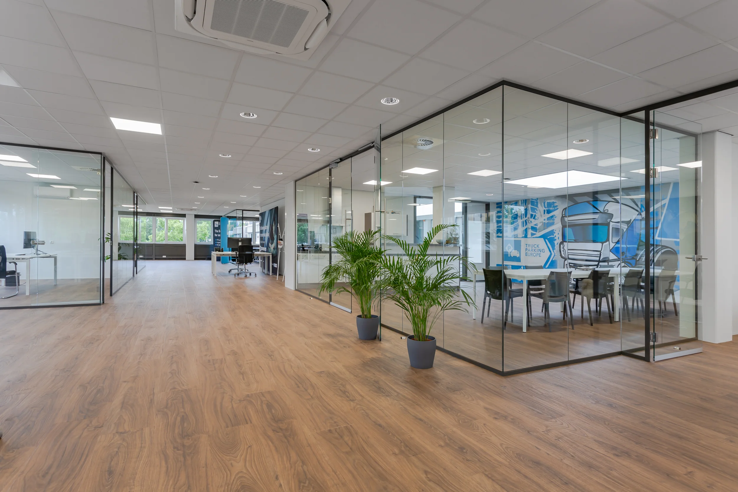 Modern kantoorinterieur met glazen vergaderruimtes, houten vloer en kamerplanten aan de Energieweg.